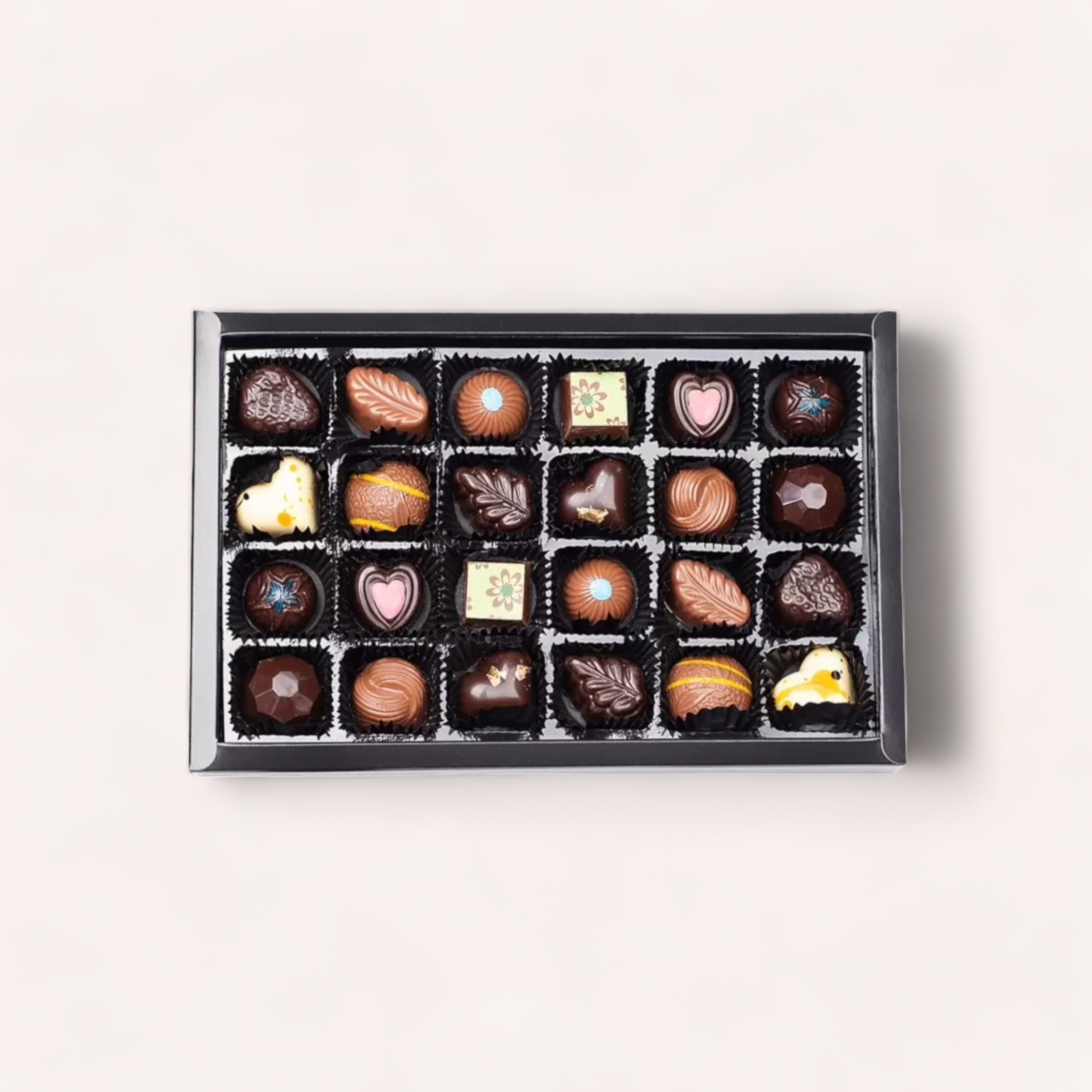 A 24 Piece Chocolate Gift Box by Chocolate Traders in various shapes and designs, including hearts and swirls, displayed neatly against a light background.