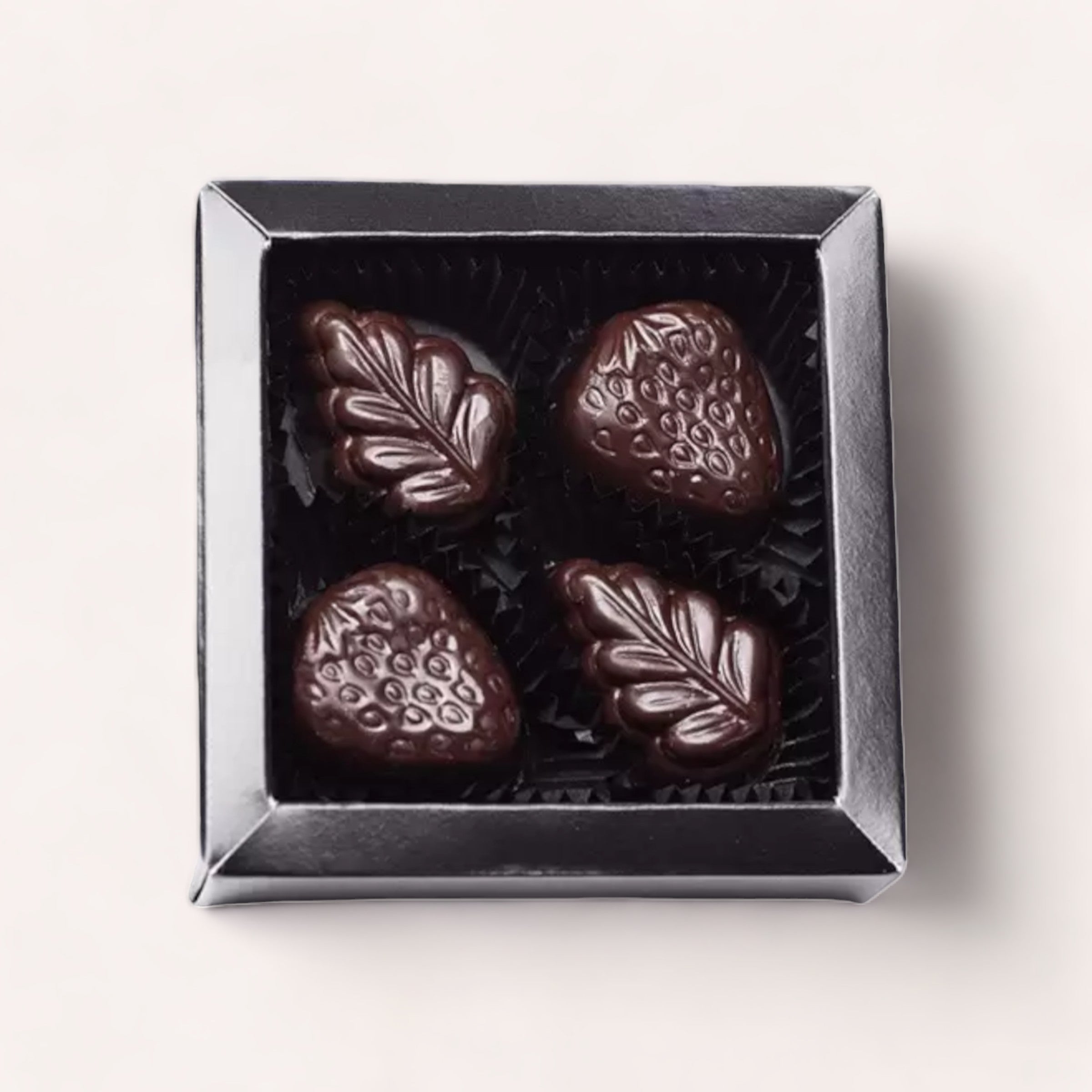 A gift box of 4 Piece Chocolate Box by Chocolate Traders, featuring artisan truffles with elegant leaf and peppermint designs, presented in a luxurious dark package.