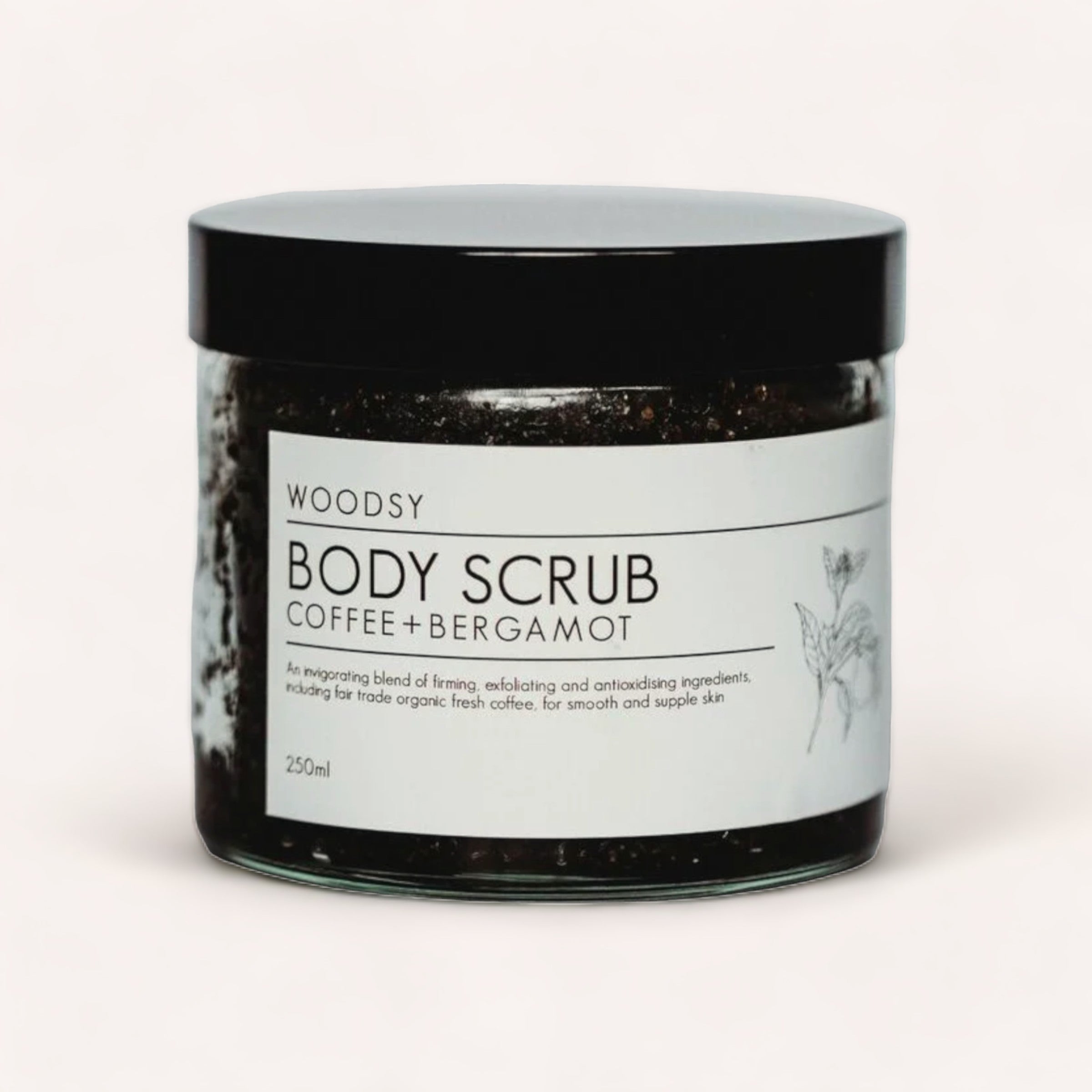 A jar of Woodsy Botanics Body Scrub - Coffee & Bergamot against a plain white background, highlighting its label and contents visibly through the clear section.