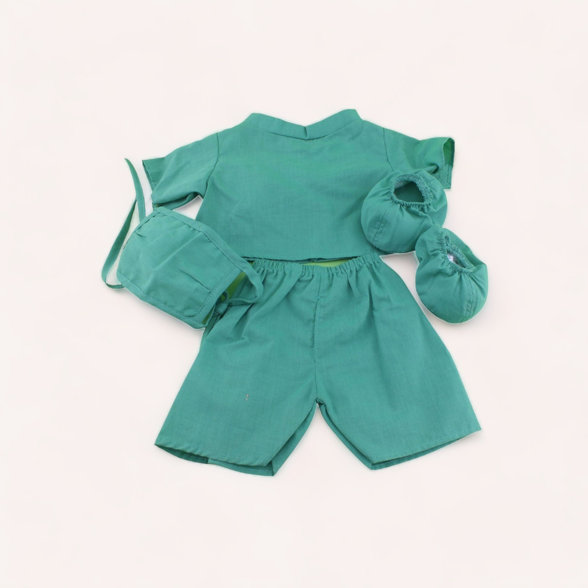 A neatly displayed set of teal baby clothes, including a shirt, shorts, and a pair of booties on a white background, perfect for imaginative play with their favorite teddy bear in The Teddy Factory's Bear Doctor Outfit.