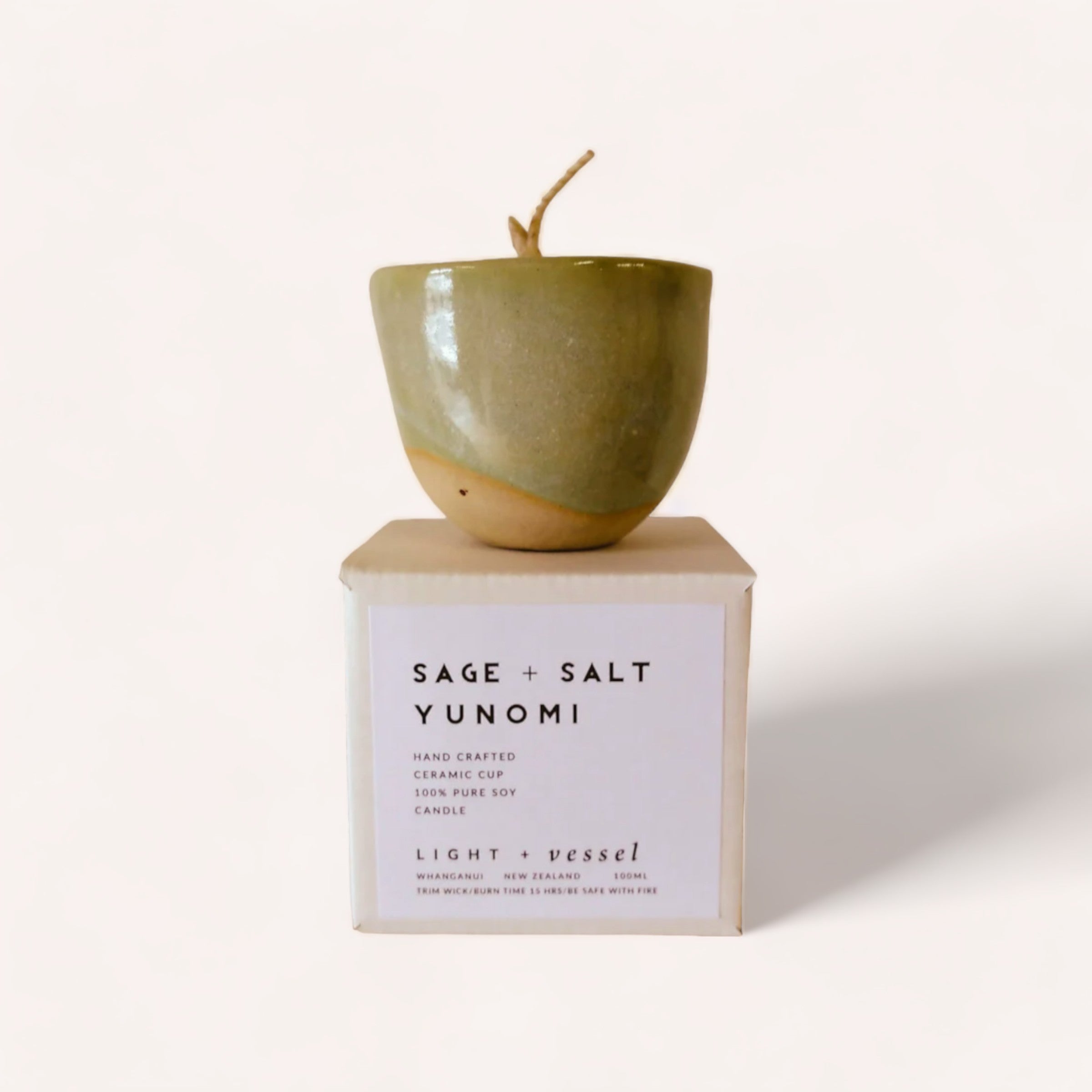 A handcrafted Sage + Salt Candle by Light + Vessel in a sage green yunomi cup, displayed on a white box labeled "sage + salt yunomi" with description texts, against a plain white background.