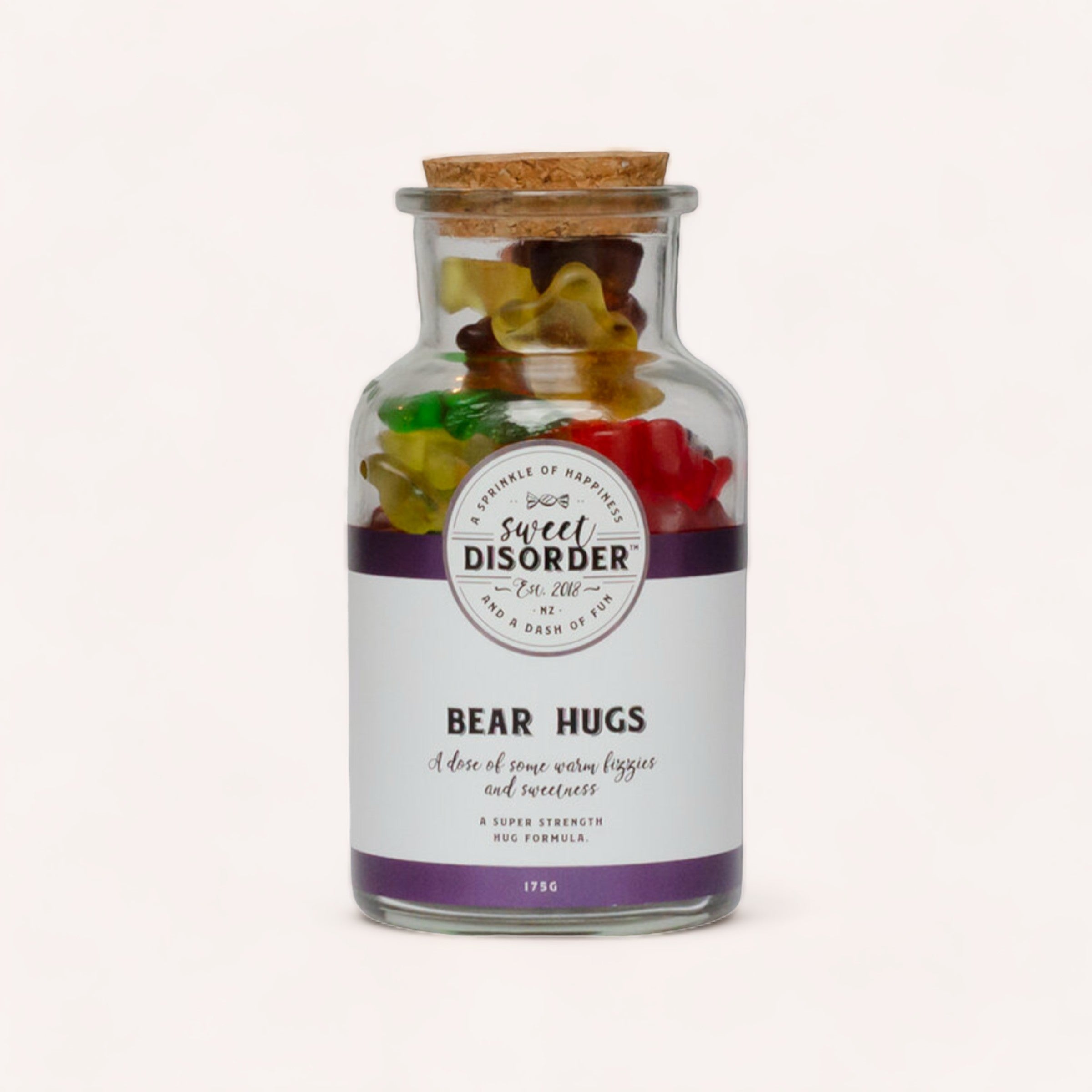 A glass jar filled with Bear Hugs Lollies by Sweet Disorder, sealed with a cork. It has a purple label that reads "super strength hugs" and encourages a dose of hugs for sweetness and strength.