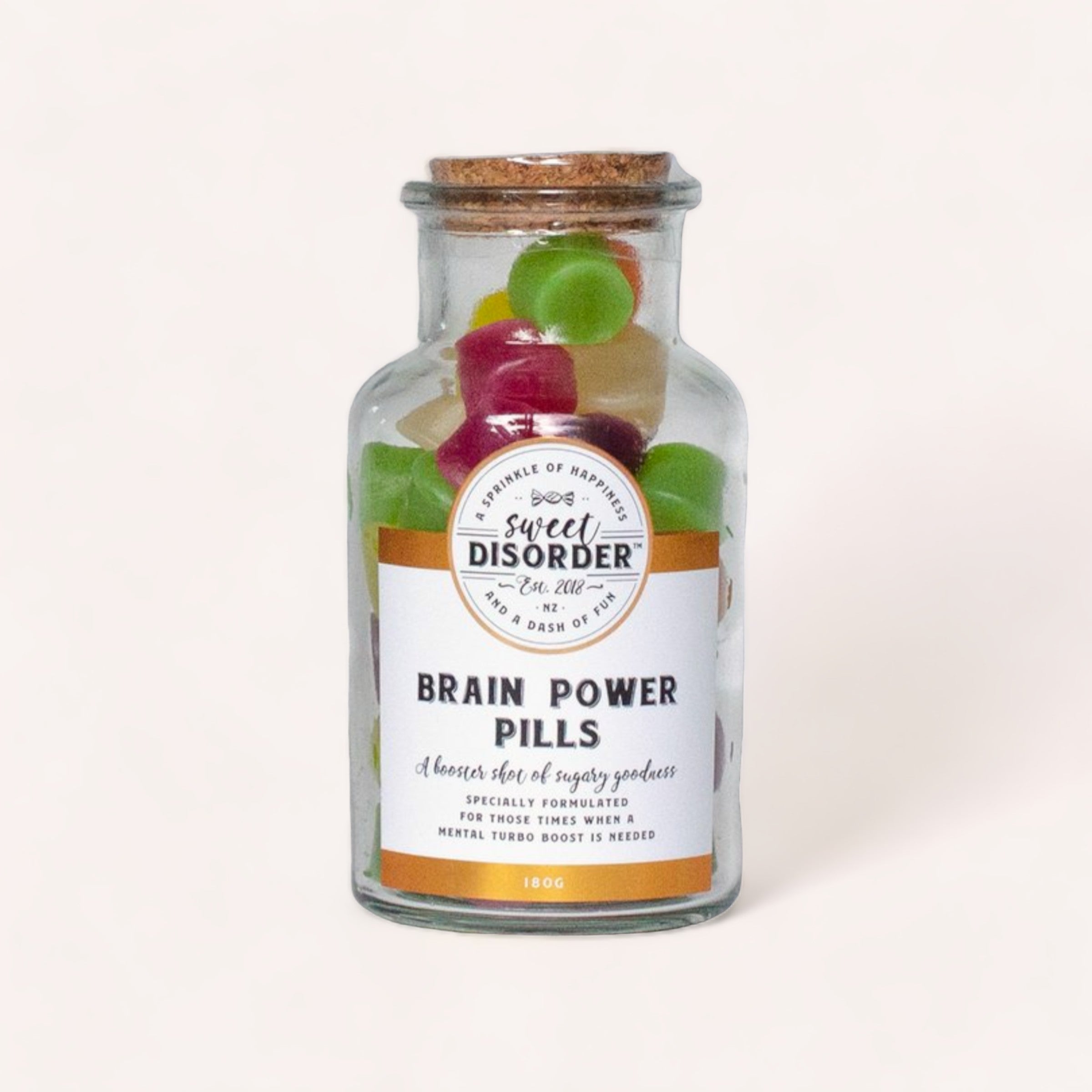 A whimsical glass jar labeled "Brain Power Pills Lollies" by Sweet Disorder, filled with colorful wine gums, playfully presented as a boost of sugary goodness for the mind.