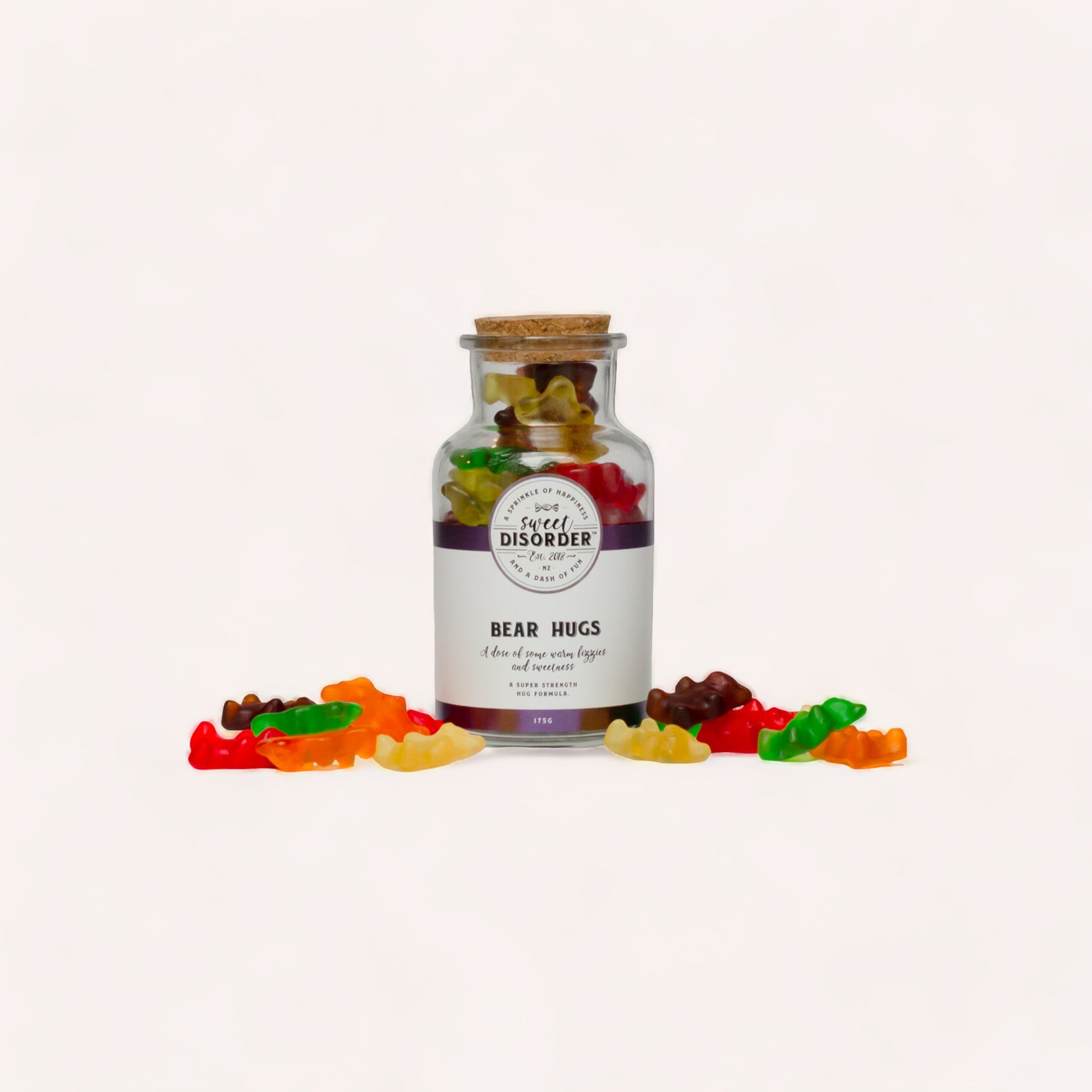 A clear glass jar labeled "Bear Hugs Lollies" by Sweet Disorder filled with colorful gummy bears, with more gummies scattered around the jar on a white background.