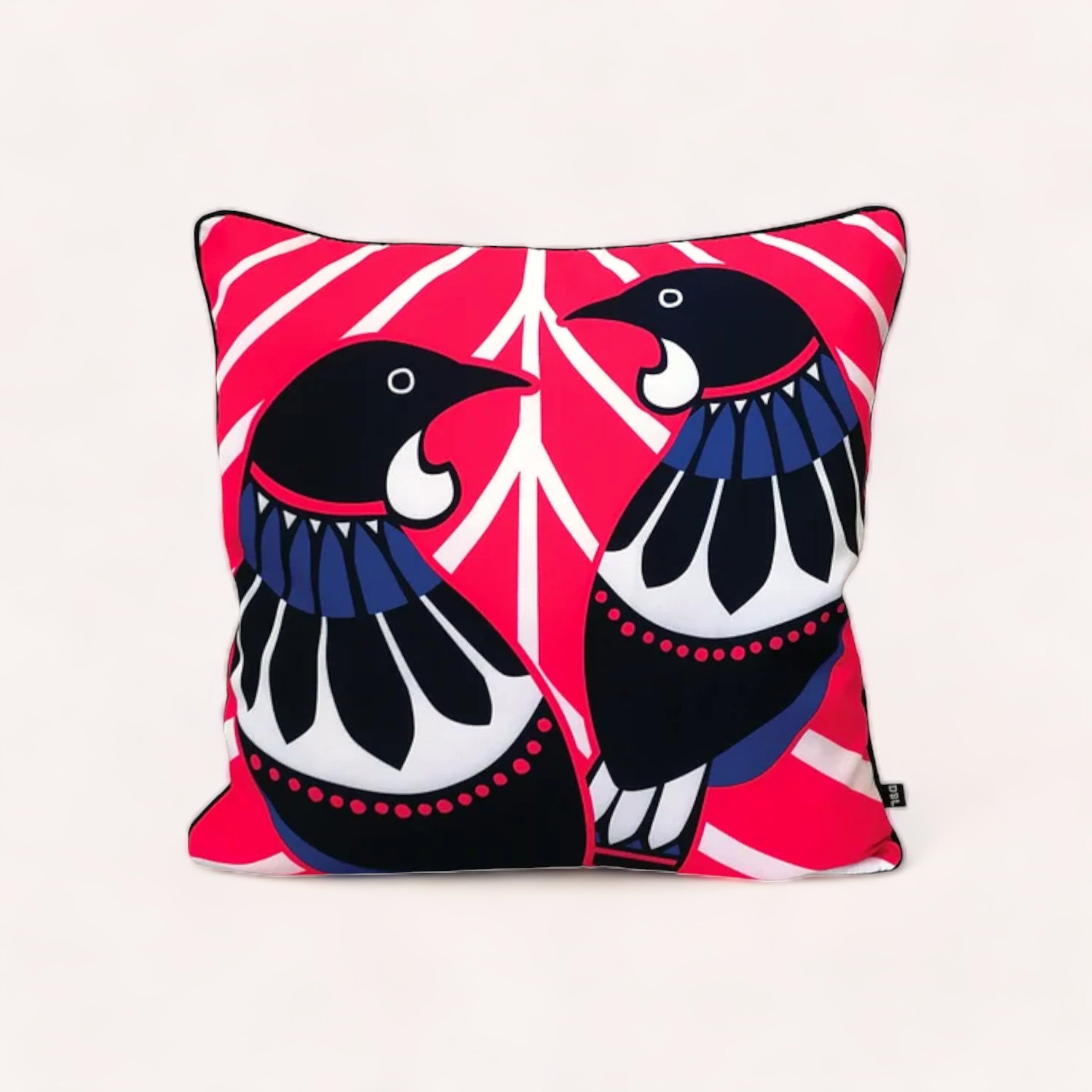 A vibrant Scandi Tui Cushion Cover crafted from canvas, featuring an abstract symmetrical pattern with two stylized NZ bird tui figures in black, white, and red against a pink background, highlighting its origin as a New Design by Leonard.