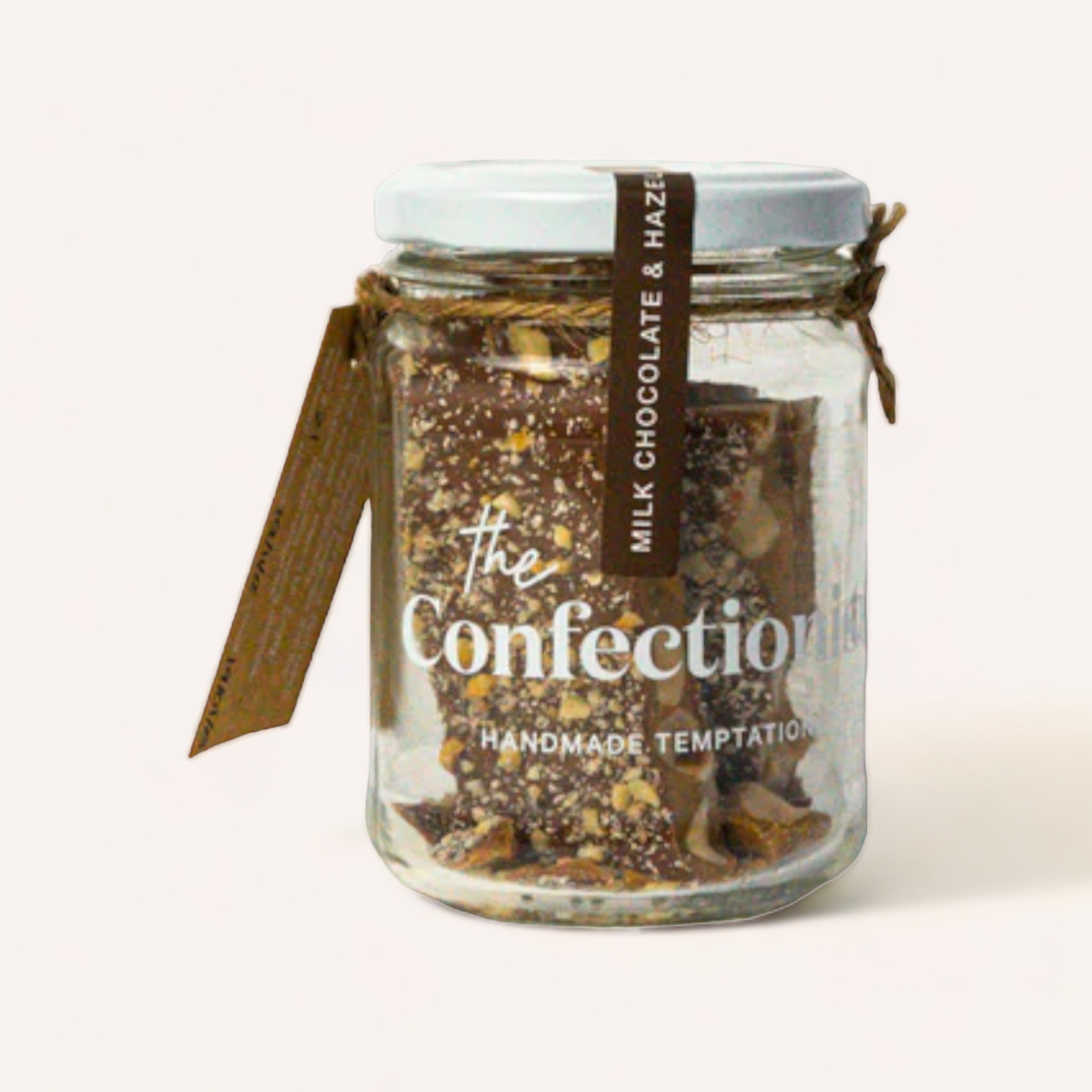 A glass jar filled with layers of Hazelnut Milk Chocolate Toffee by The Confectionist, labeled "the confection," tied with a brown ribbon.