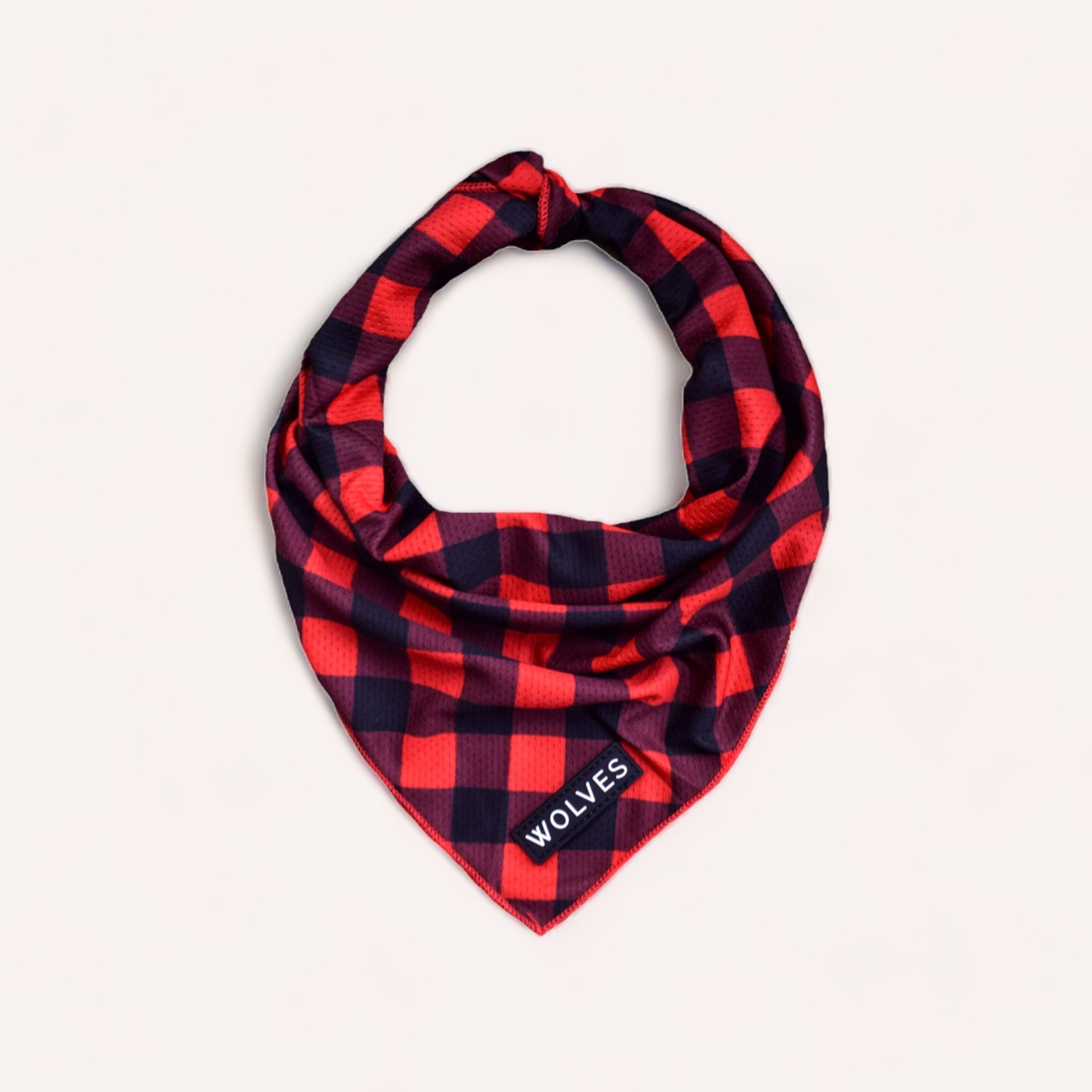 A Buffalo Bandana by Wolves of Wellington, a red and black checkered, wrinkle-free bandana with the word "wolves" embroidered at one corner, neatly folded into a triangle and placed against a pale background, perfect for dog band.