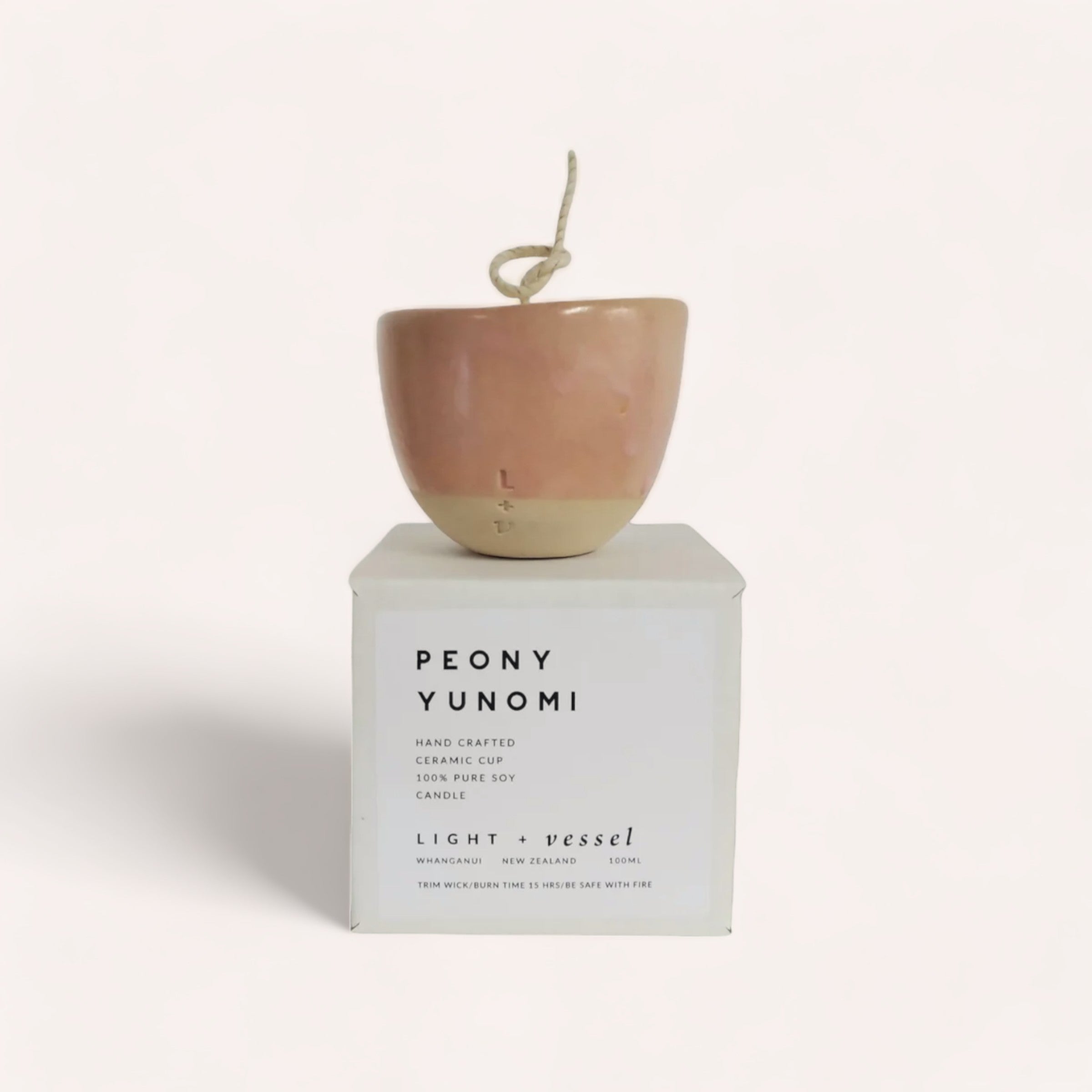 A ceramic Peony Candle by Light + Vessel with a wick, displayed on its packaging labeled "Peony Candle by Light + Vessel, handcrafted, coconut soy candle with natural fragrance oils, light + vessel".