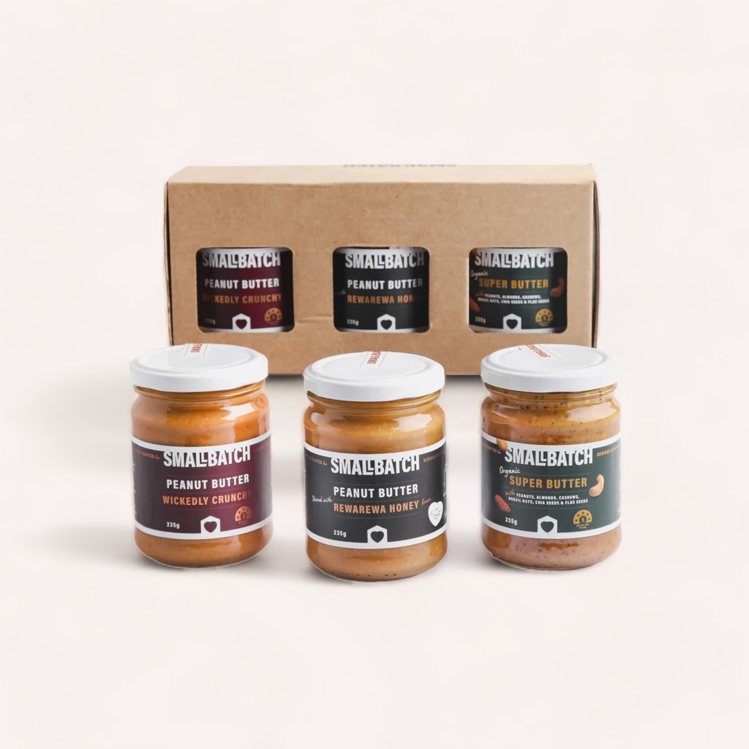 A variety of gourmet Smallbatch Peanut Butter Gift Boxes from New Zealand in front of their brown packaging box, showcasing different textures like smooth, crunchy, and super butter.