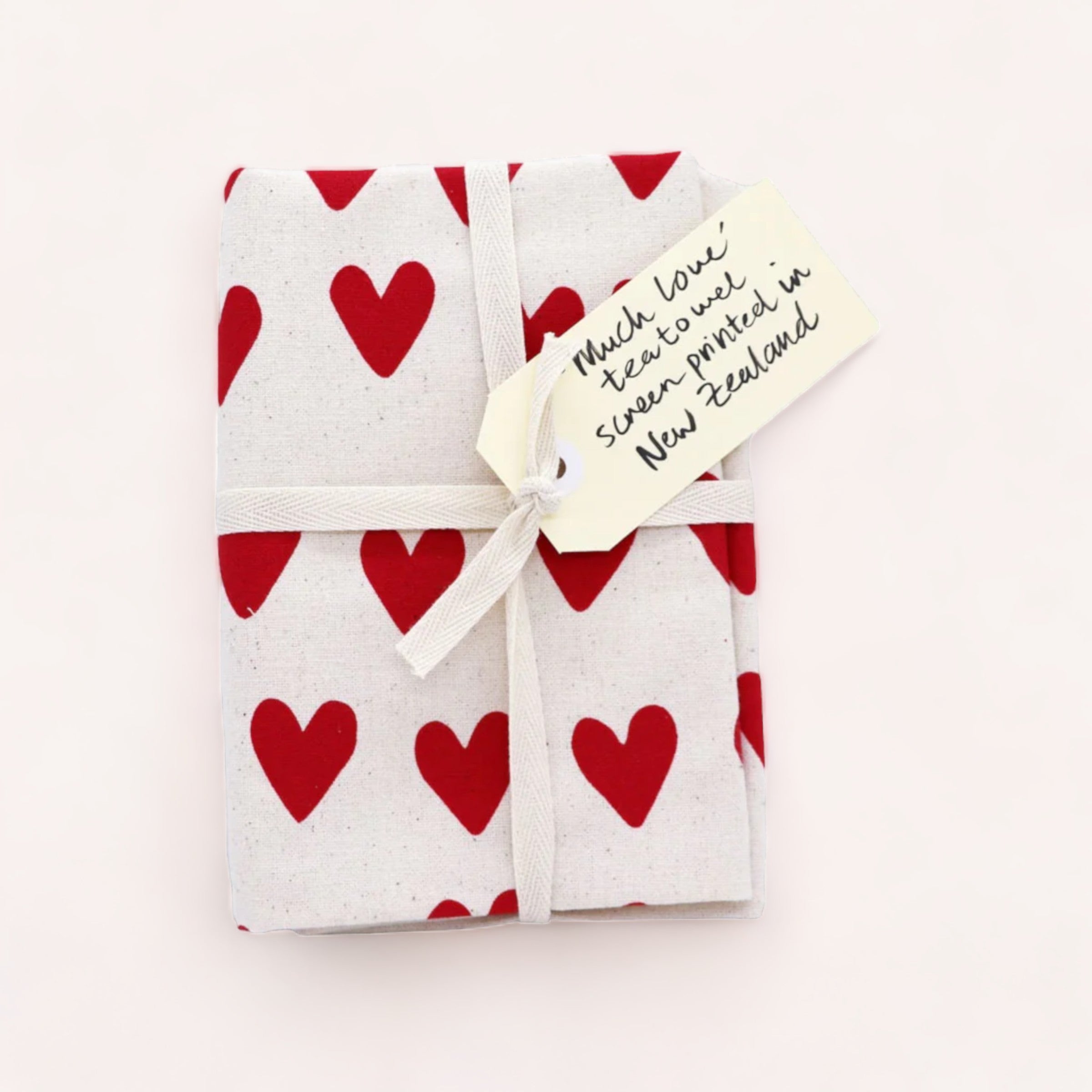A gift wrapped in heart-patterned paper tied with a white ribbon, accompanied by a handwritten note on a Much Love Tea Towel from Tuesday Print that says, "thank you. Steaks tasted