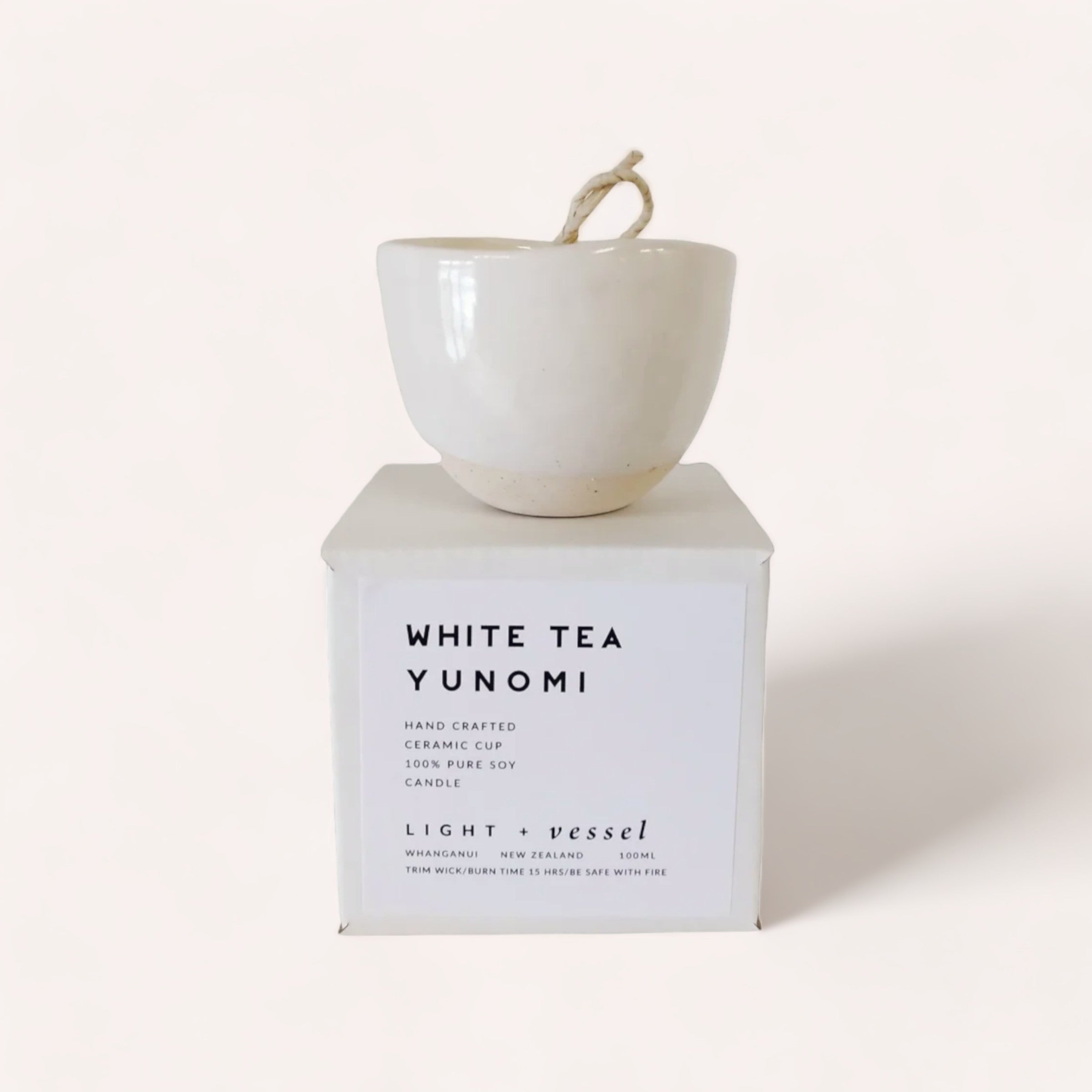 A white ceramic yunomi-style cup placed on top of its packaging box, which is labeled as a "White Tea Candle" by "Light + Vessel" with the