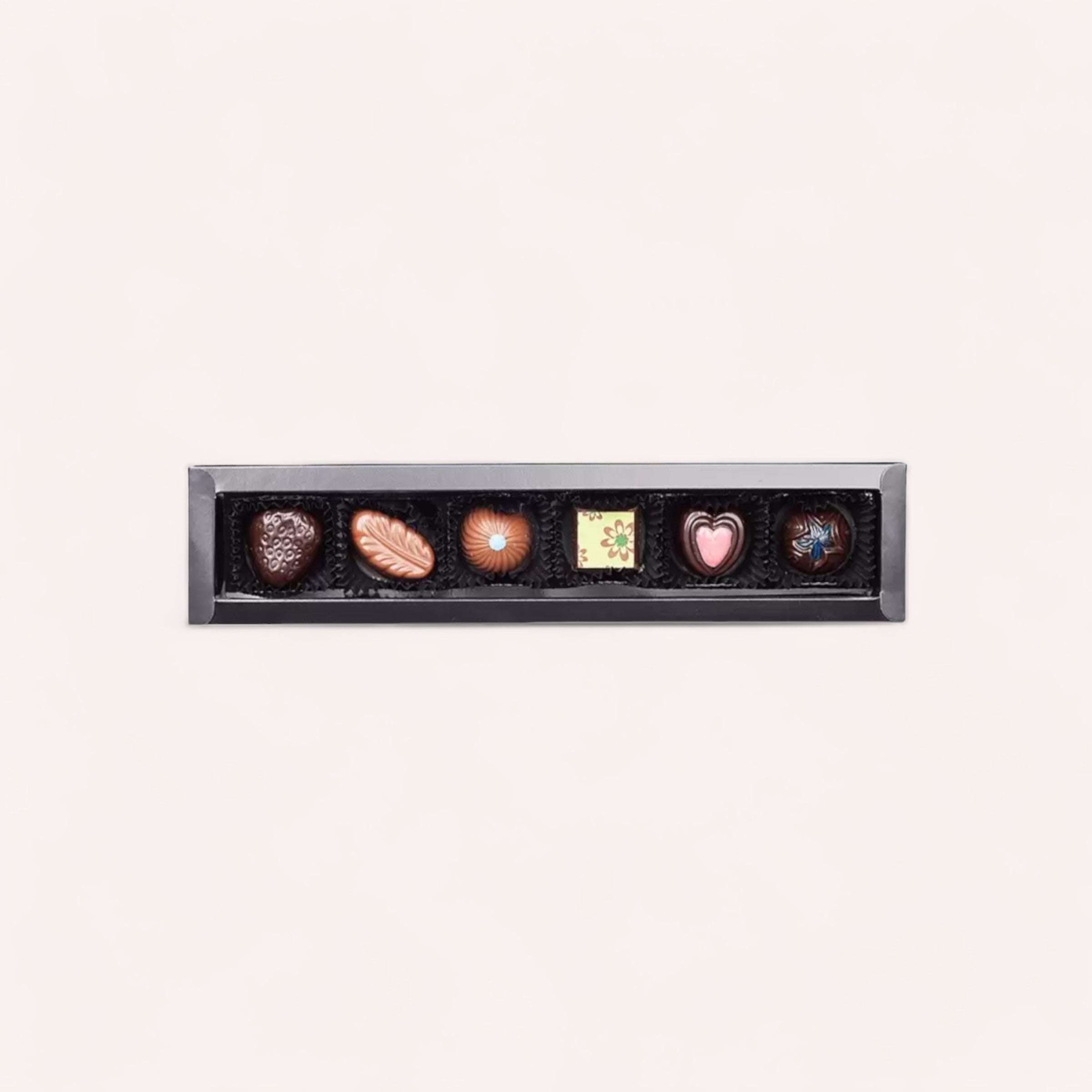 A selection of Chocolate Traders' 6 Piece Chocolate Box, featuring gourmet New Zealand chocolates in a sleek black box, intricate designs, and a colorful heart-shaped piece, eloquently presented against a clean, white background.