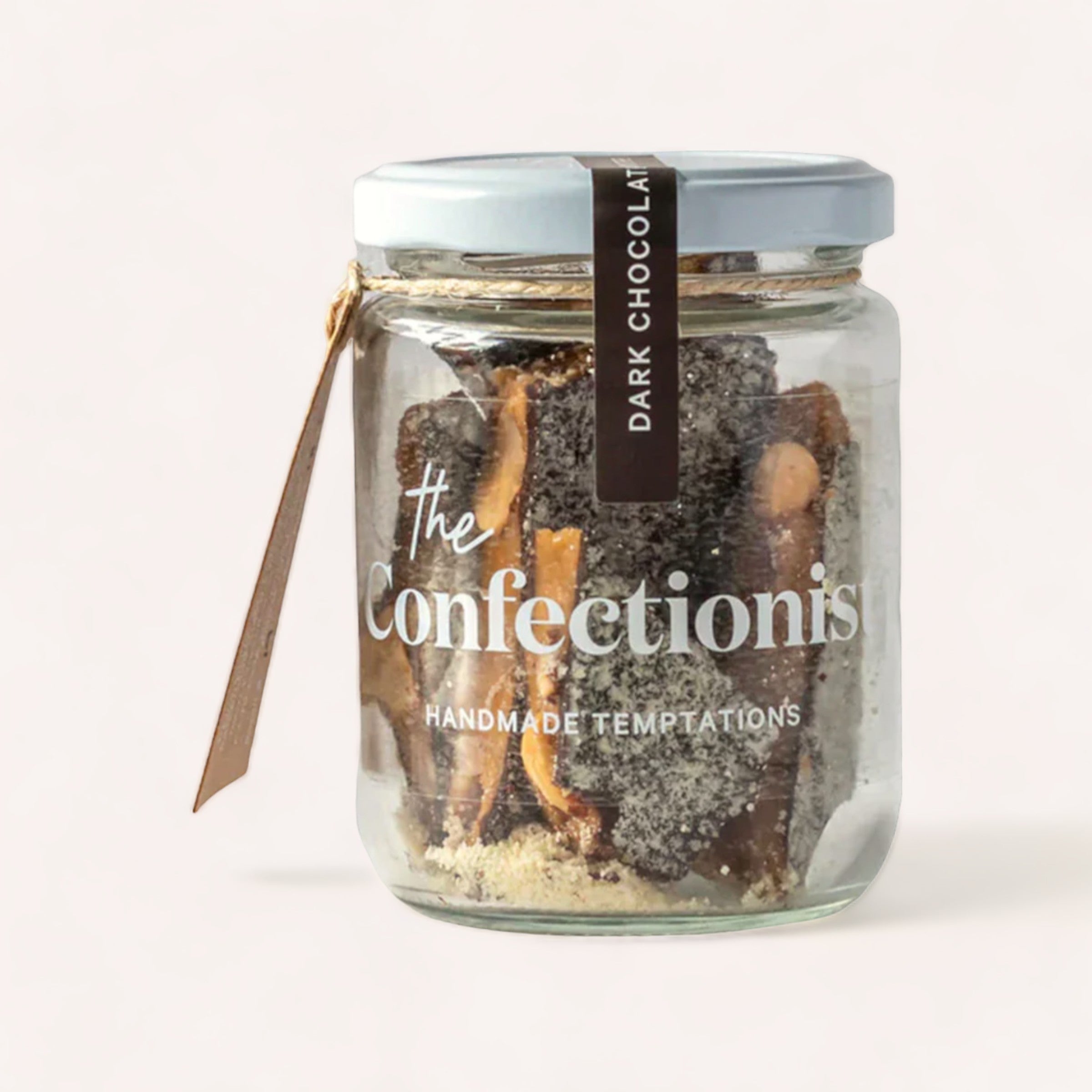 A clear glass jar containing Almond Dark Chocolate Toffee by The Confectionist, labeled "the confectionist - handmade temptations", sealed with a silver lid and decorated with a brown ribbon.