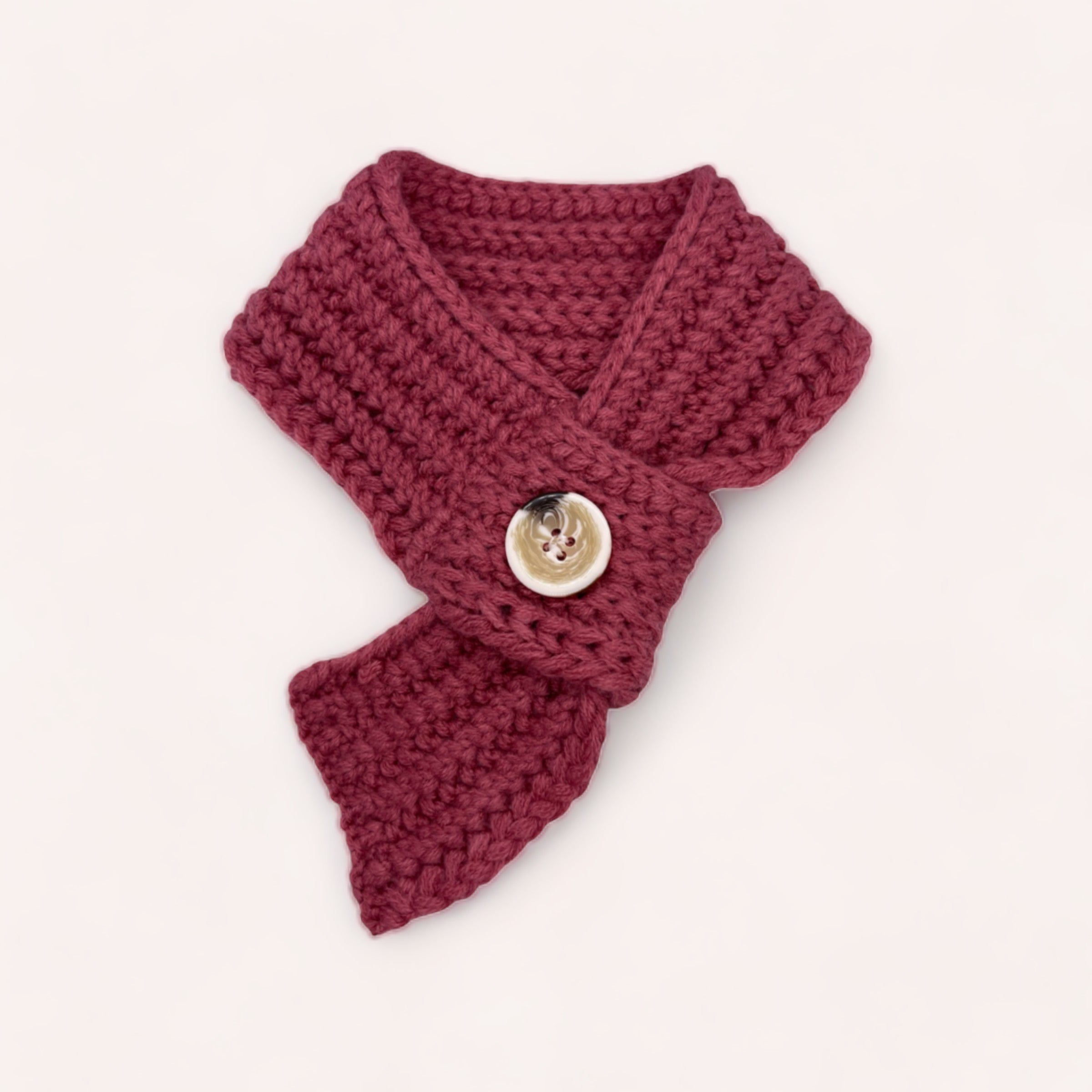A handcrafted maroon acrylic Pet Scarf with a decorative button laying on a white background, perfect as a pet winter accessory from giftbox co.