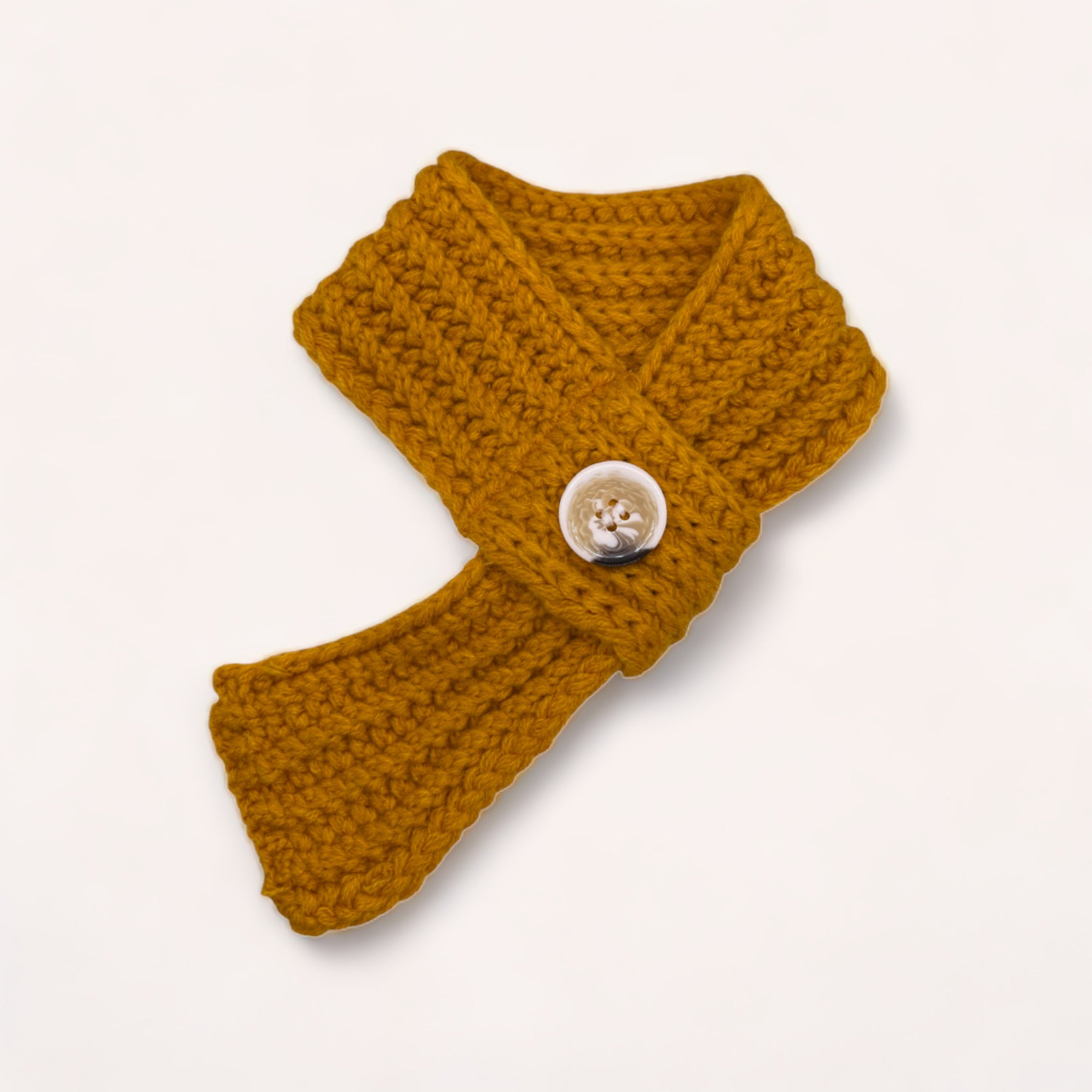 A mustard yellow crochet pet scarf with a button detail, perfect as a winter accessory for your furry friend, displayed on a white background by giftbox co.