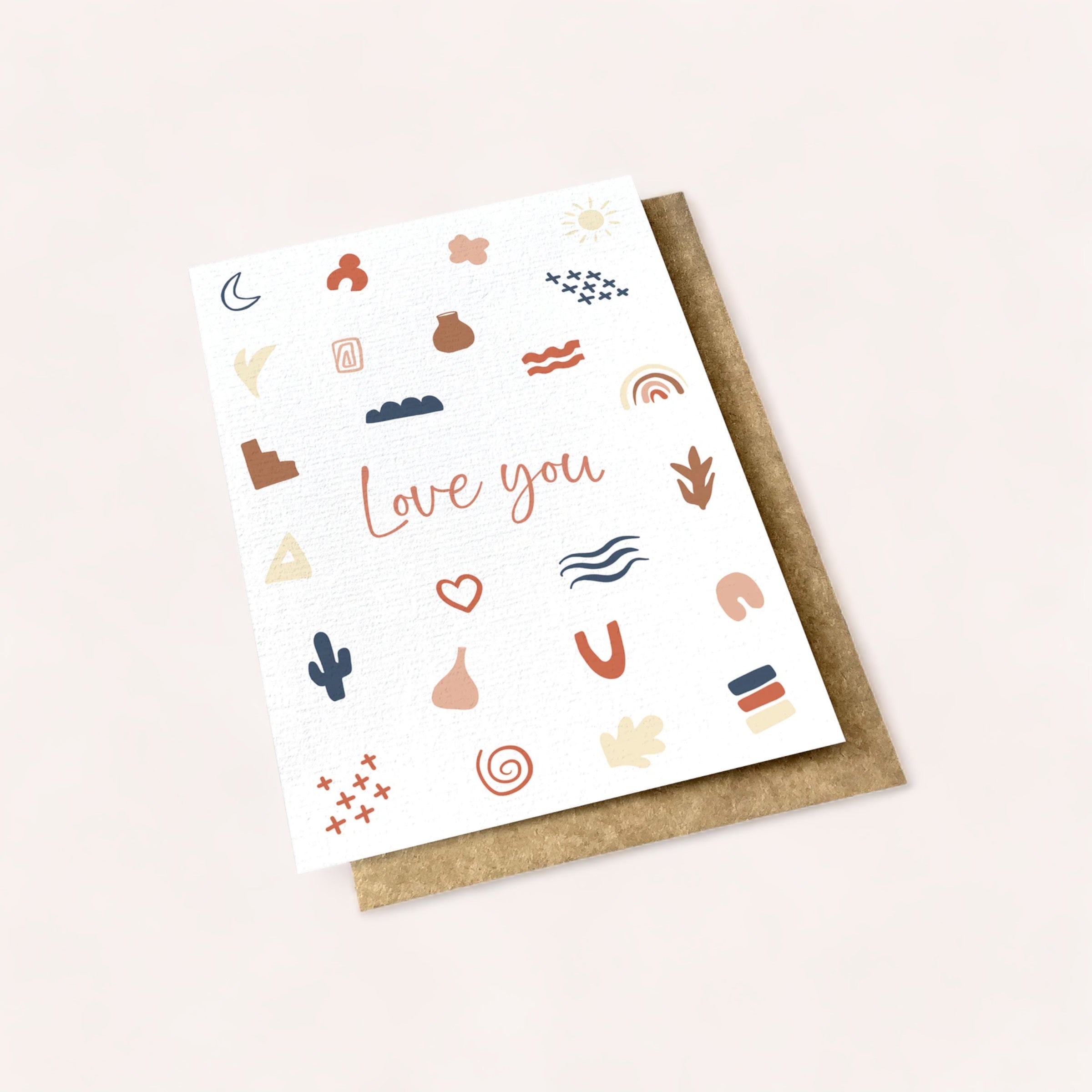 A delicate and artistic Ink Bomb Love You Card, part of a multibuy collection, with the phrase "love you" surrounded by various whimsical symbols and shapes, presented on a cream background with a natural textured.