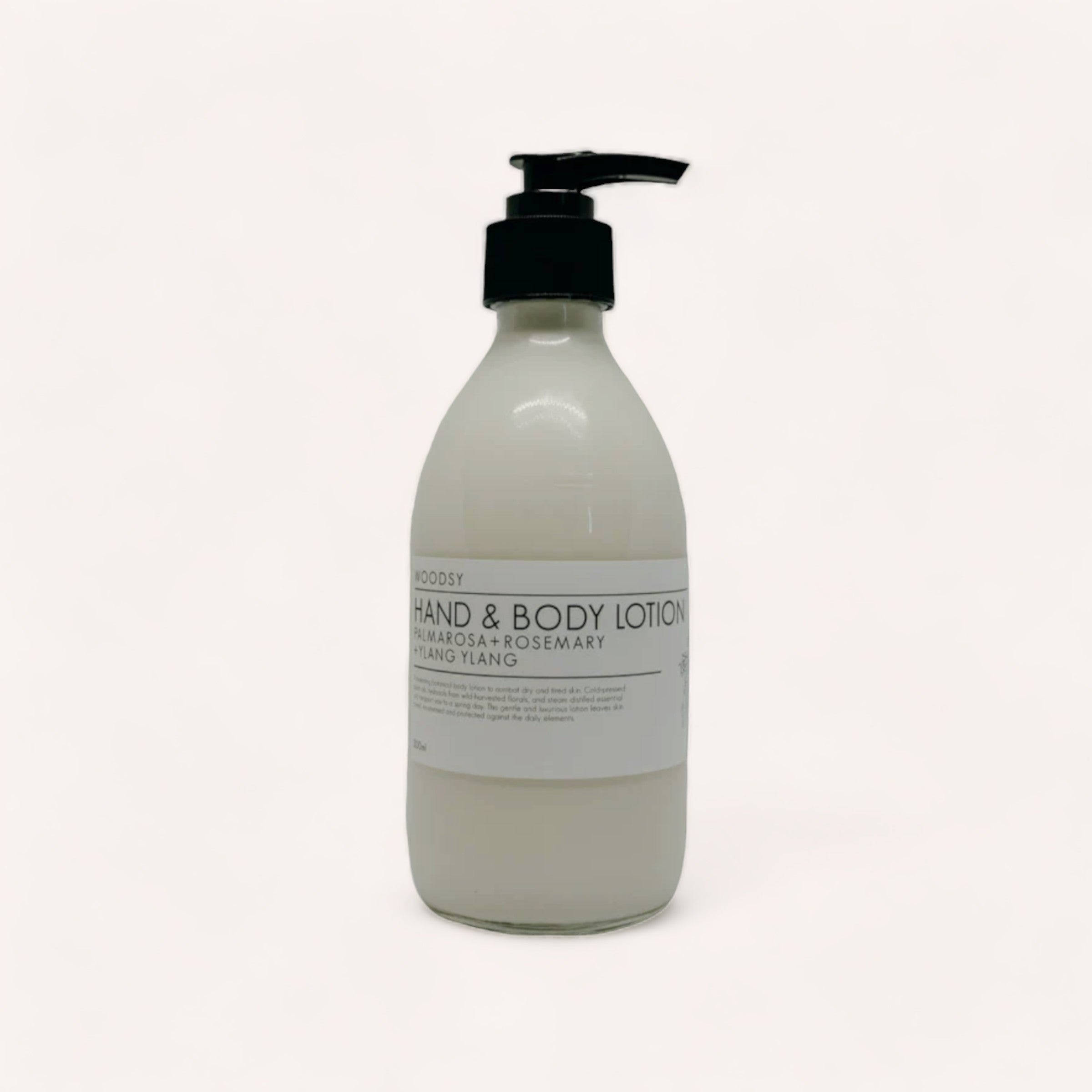 A pump bottle of Hand & Body Lotion - Palmarosa & Ylang Ylang by Woodsy Botanics with lavender and rosemary essential oils on a white background.