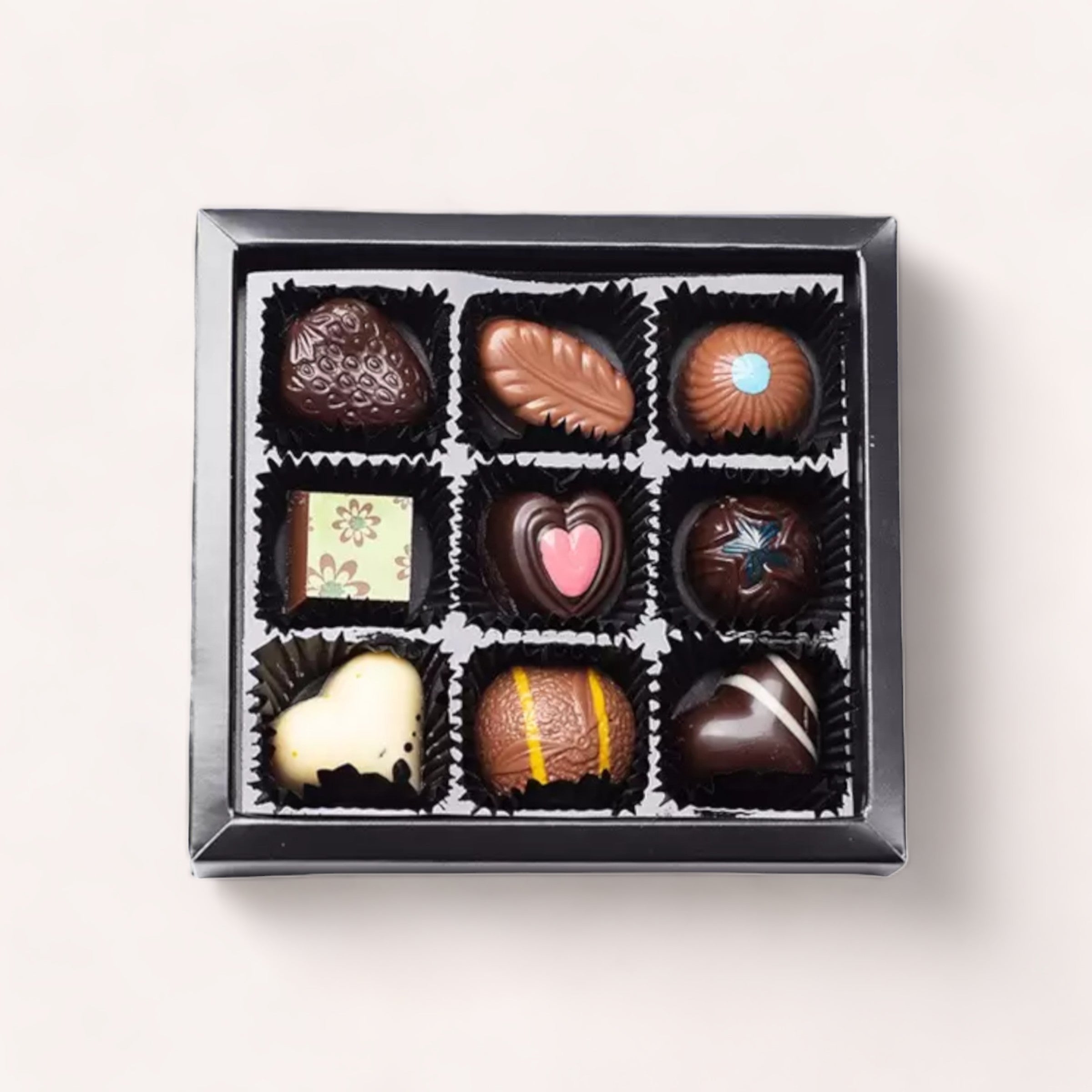 A 9 Piece Chocolate Gift Box by Chocolate Traders with various shapes and designs including hearts and flowers, displayed against a light grey background.