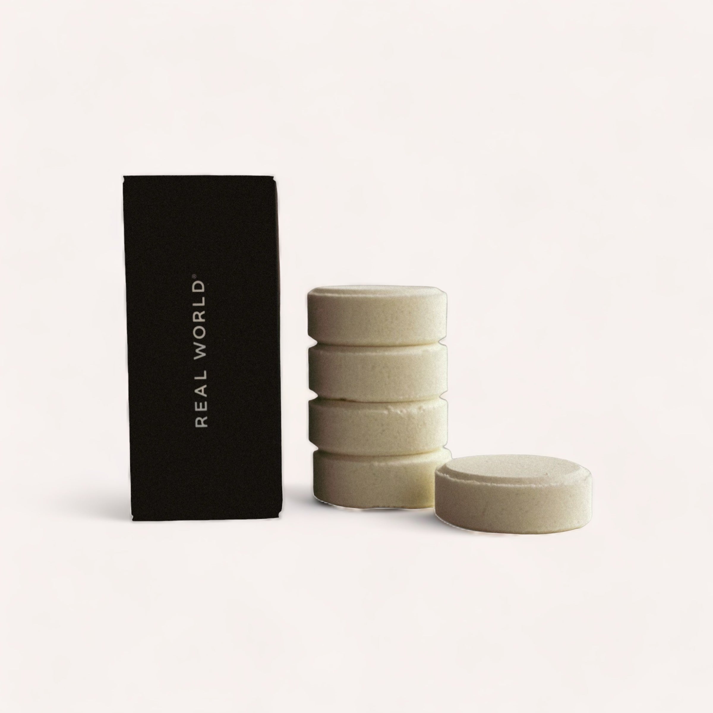 A stack of four natural-colored lemongrass Shower Steamers by Real World solid shampoo bars next to a single bar, with an elegant black packaging labeled "Aroma Koromiko.
