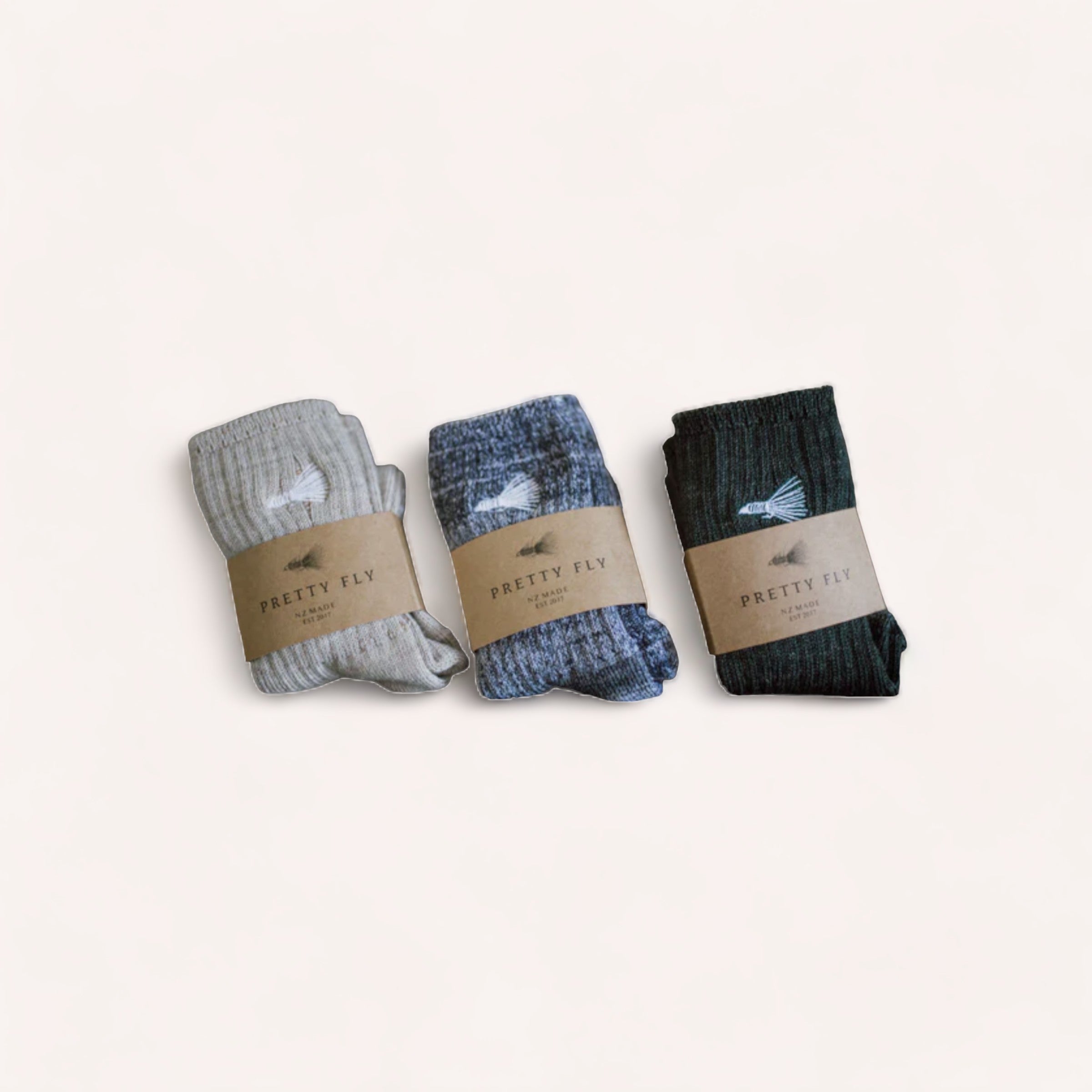 Three pairs of neatly folded Marino Wool Socks by Pretty Fly in varying shades of gray and blue, each with a label reading "pretty fly," presented against a clean, light background.