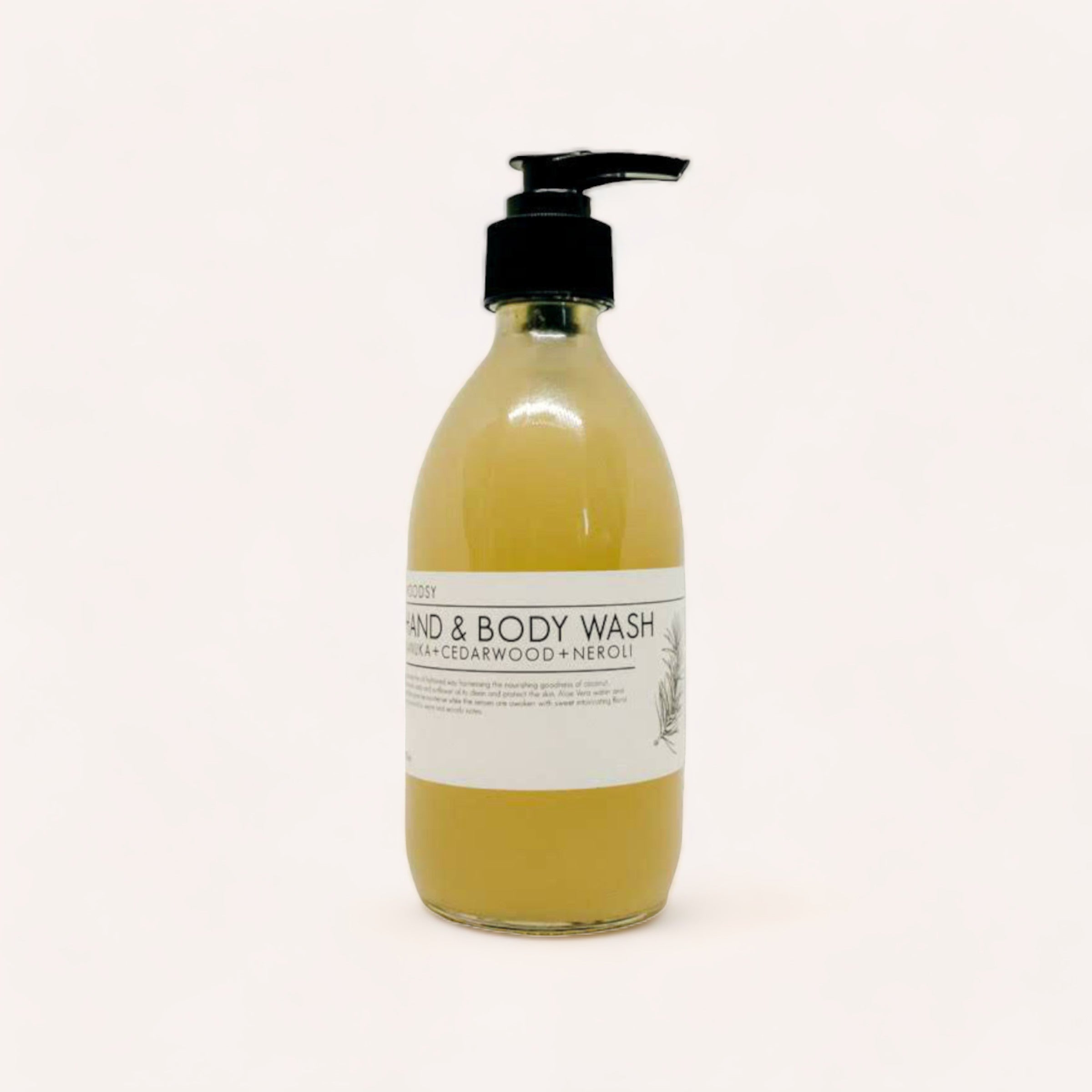 A transparent bottle of Hand & Body Wash - Kanuka, Cedarwood & Neroli by Woodsy Botanics, liquid hand and body wash with a black pump dispenser on a white background, featuring Aloe Vera water.