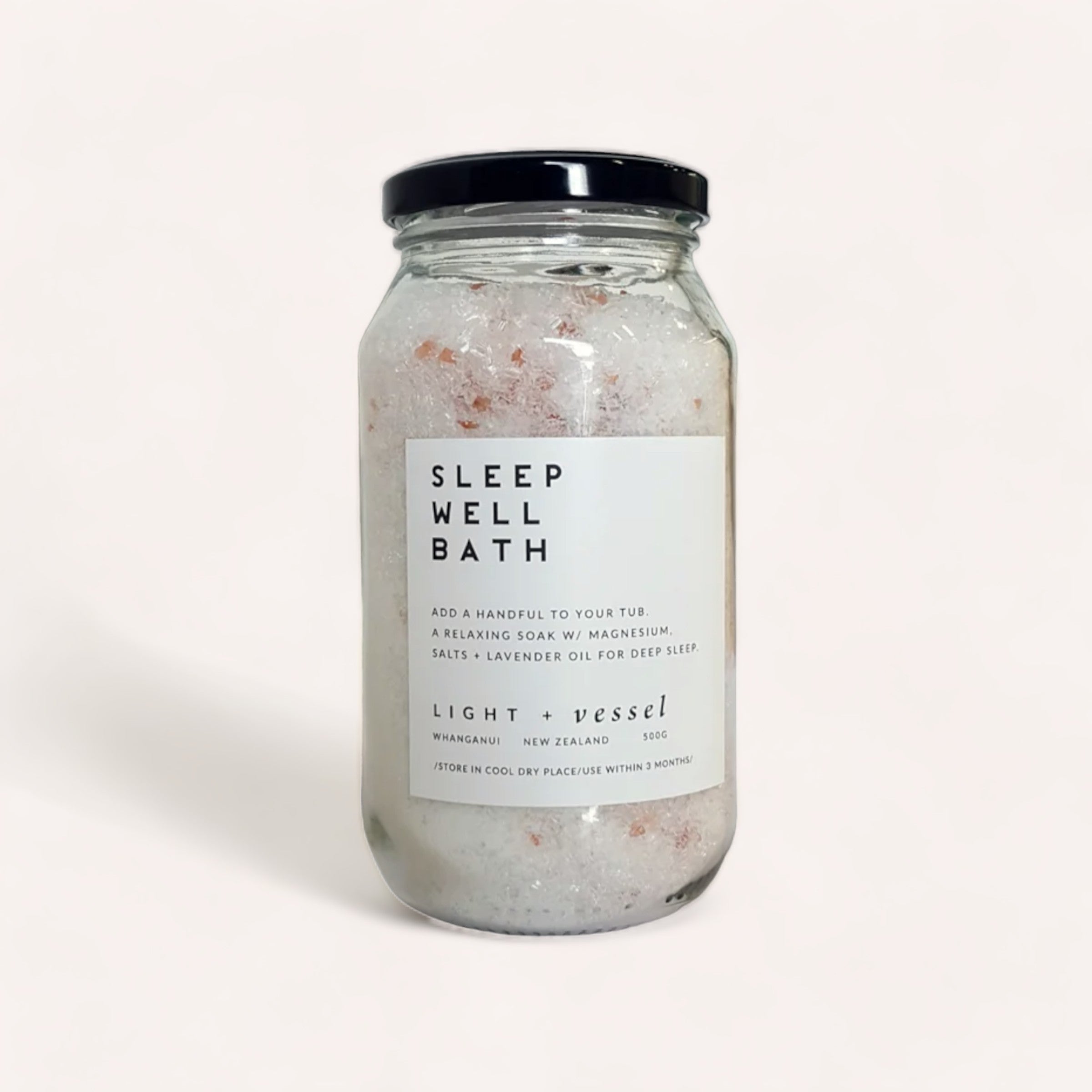 A jar of "Sleep Well Bath" bath salts with essential oils of lavender and magnesium pink mountain salts, designed for relaxation and sleep enhancement, produced by Light + Vessel from Whanganui, New Zealand.