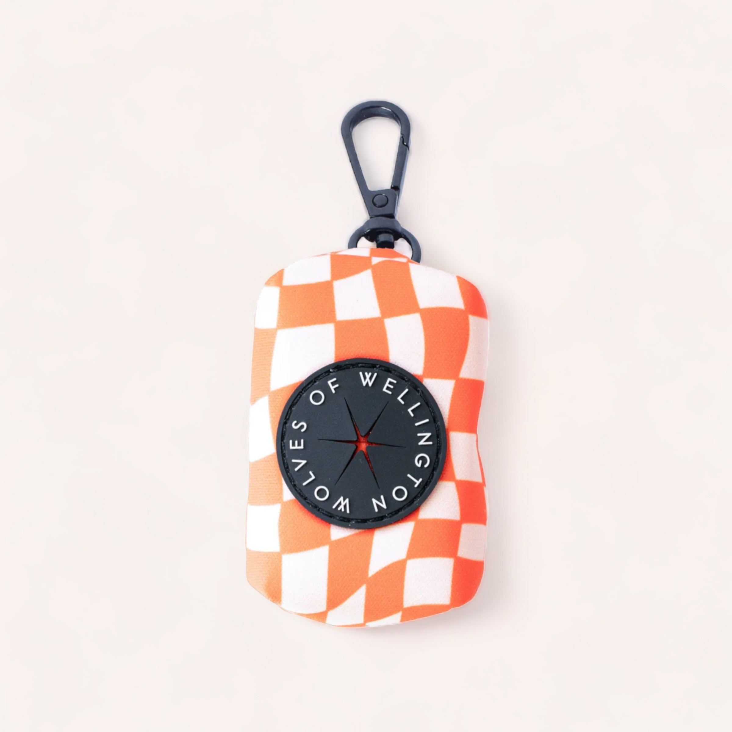 A portable, checkered orange and white patterned Benji Poop Pouch by Wolves of Wellington with a black carabiner clip and a logo stating "voices of wellington" against a beige background.