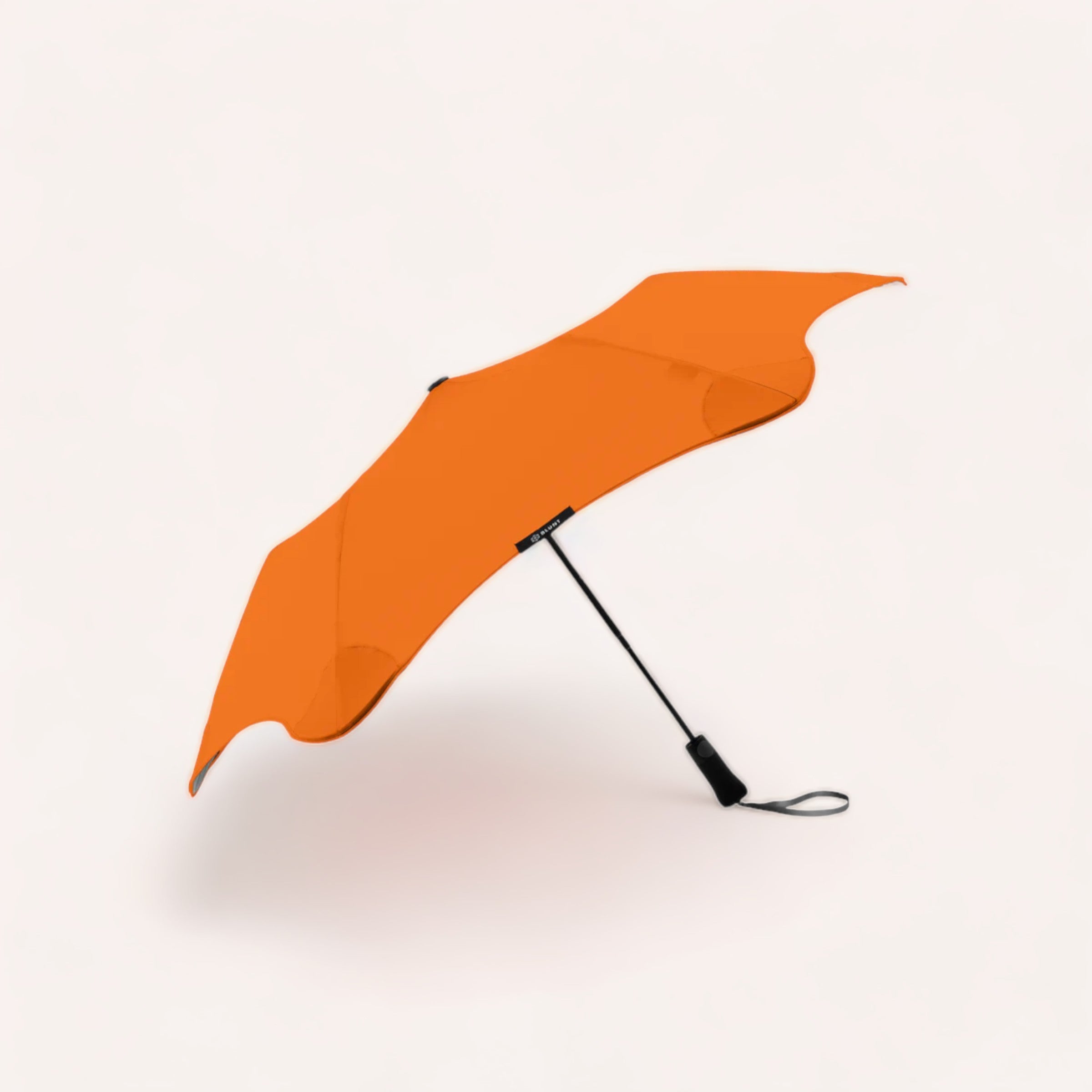 A vibrant orange BLUNT Metro umbrella with an auto-open canopy, open and resting sideways against a white background.
