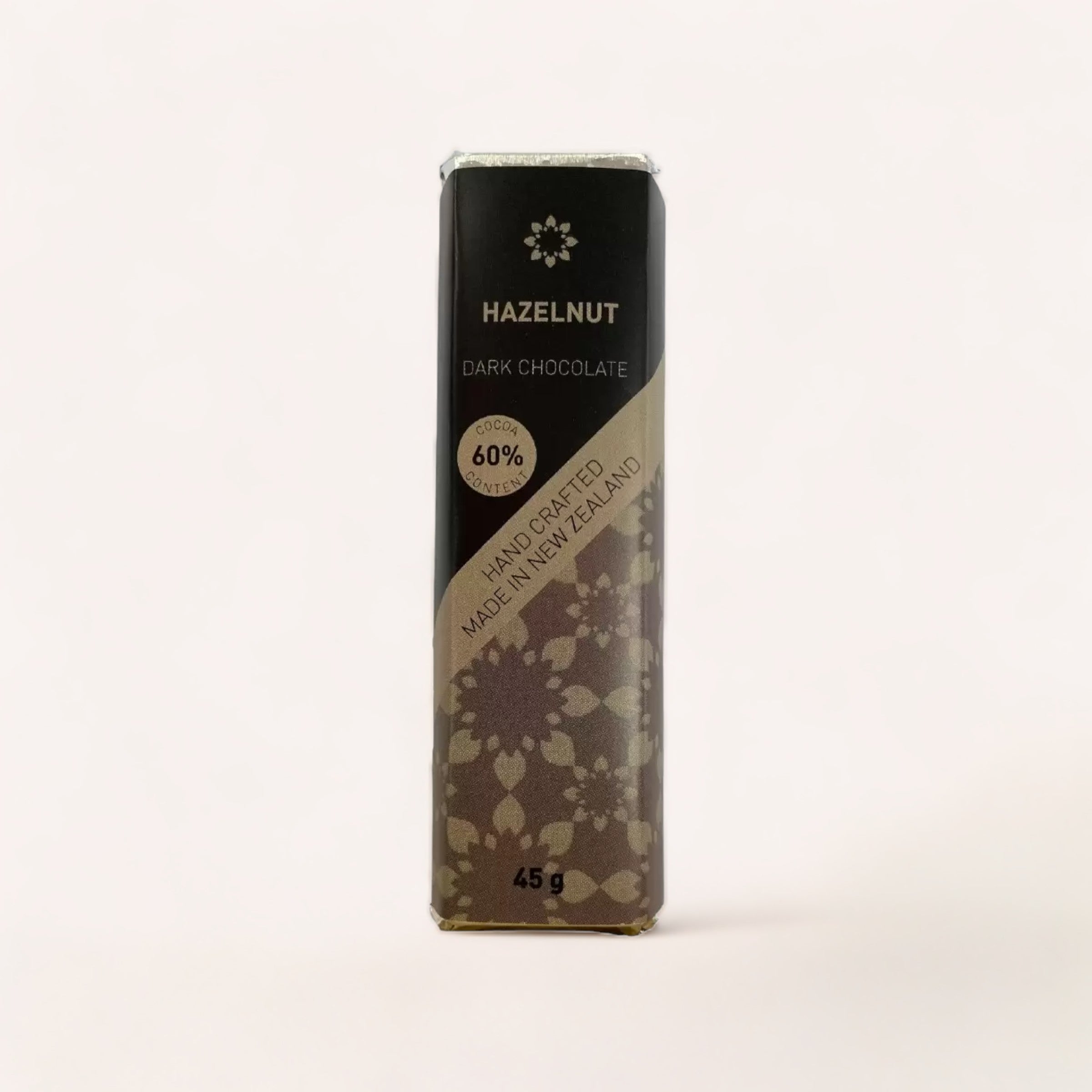 A hand-crafted bar of Hazelnut Chocolate bar by Chocolate Traders with 60% cocoa, Product of New Zealand, elegantly wrapped in a package with floral motifs.