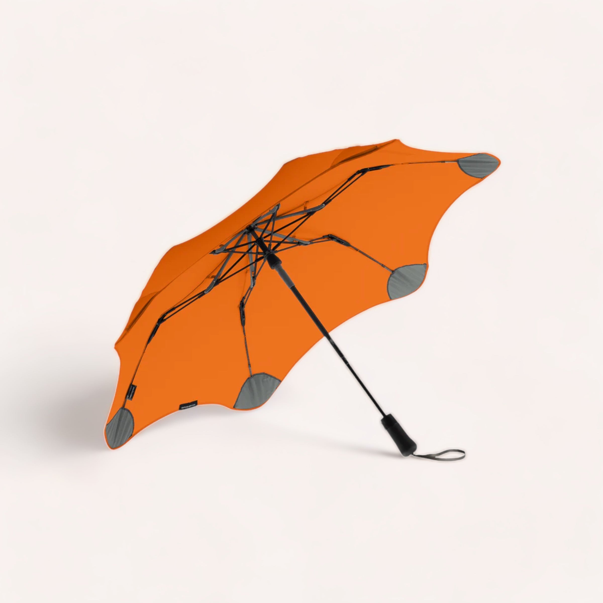 A bright orange BLUNT Metro umbrella turned inside out against a white background, likely depicting a windy day scenario for an urban dweller.
