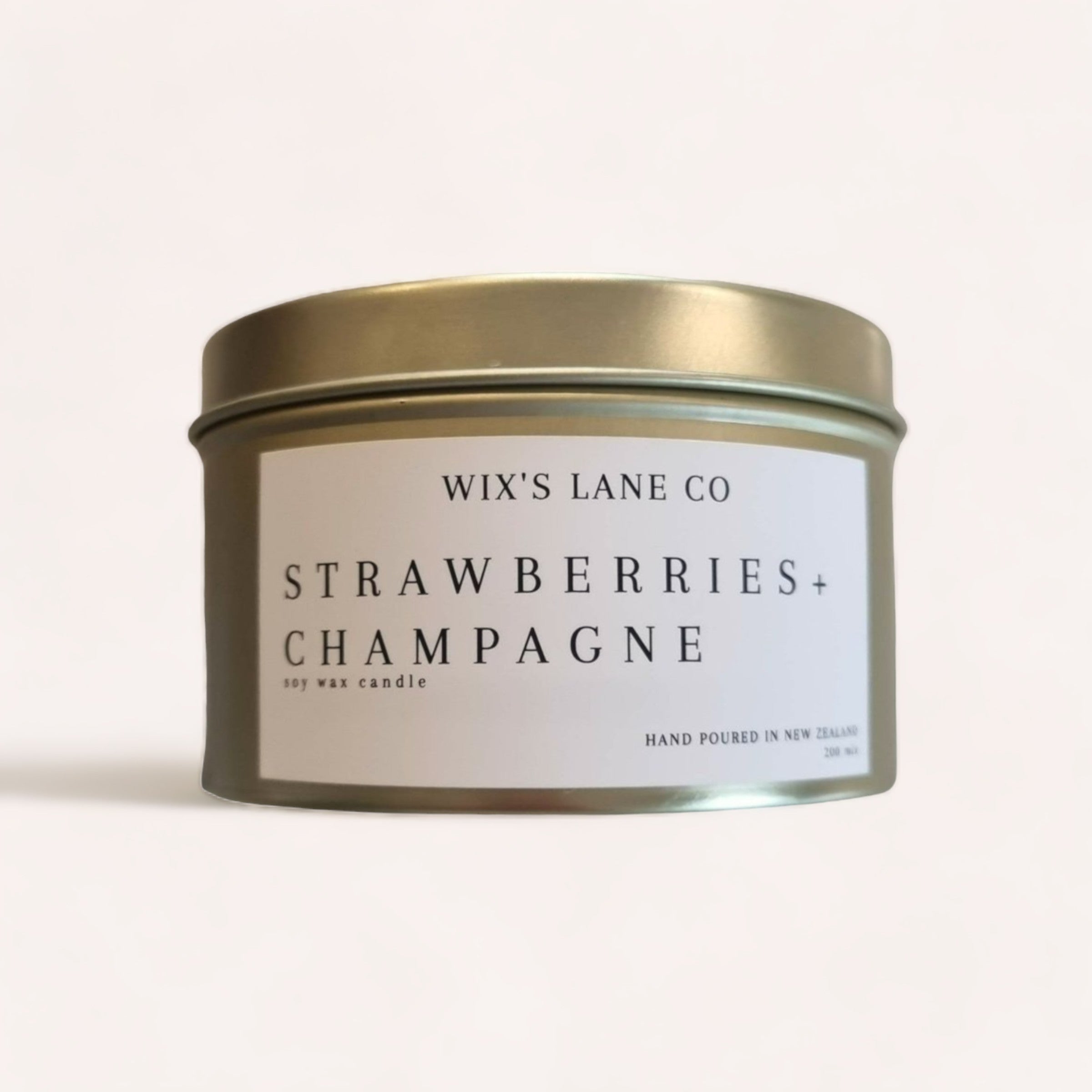 A Strawberries + Champagne Candle by Wix's Lane Co. with a soy wax, hand-poured in New Zealand, presented in a reusable gold tin against a clean, neutral background.