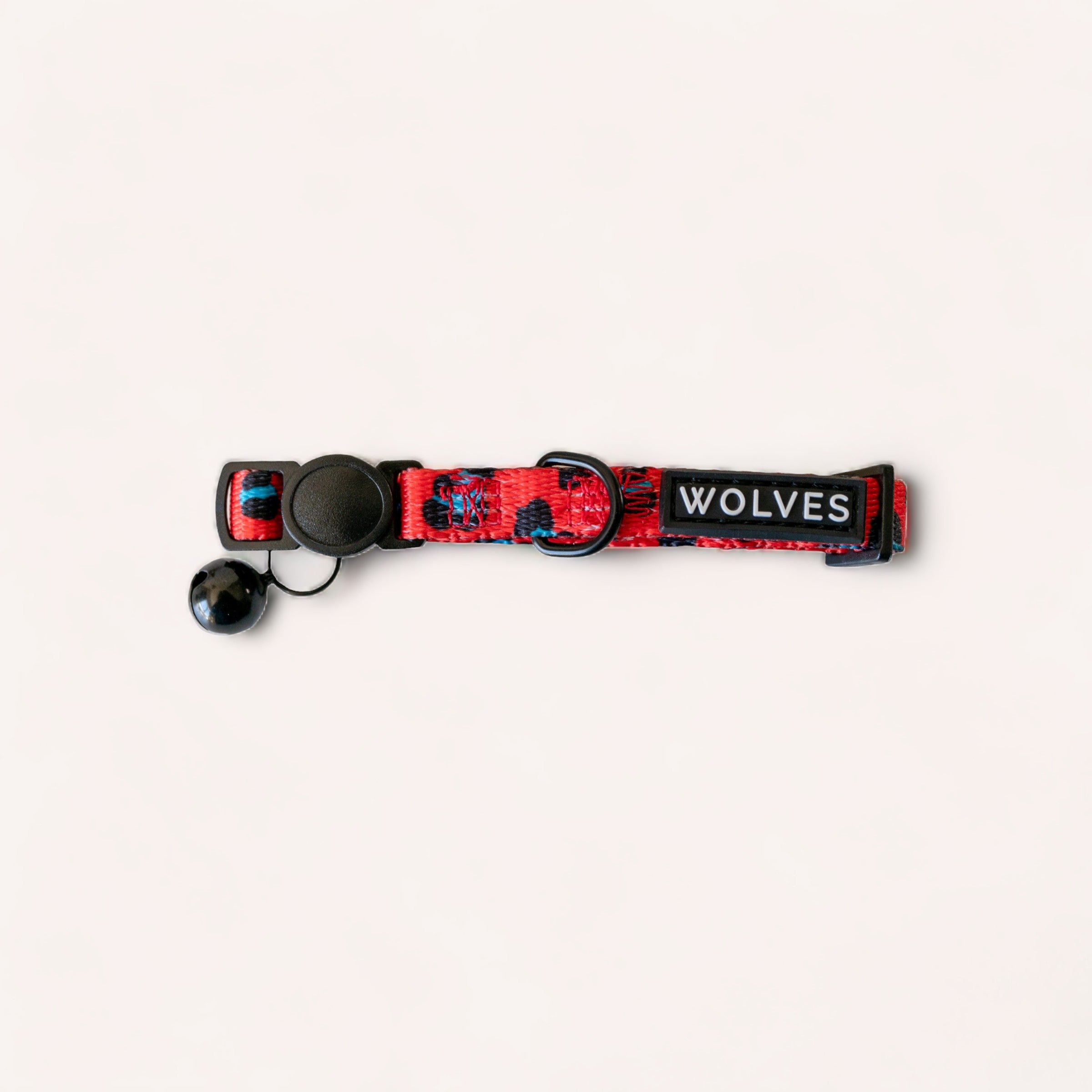A red and black patterned Cleo Cat Collar by Wolves of Wellington with "wolves" text and an attached silver bell, featuring a breakaway buckle, laid out on a plain white background.