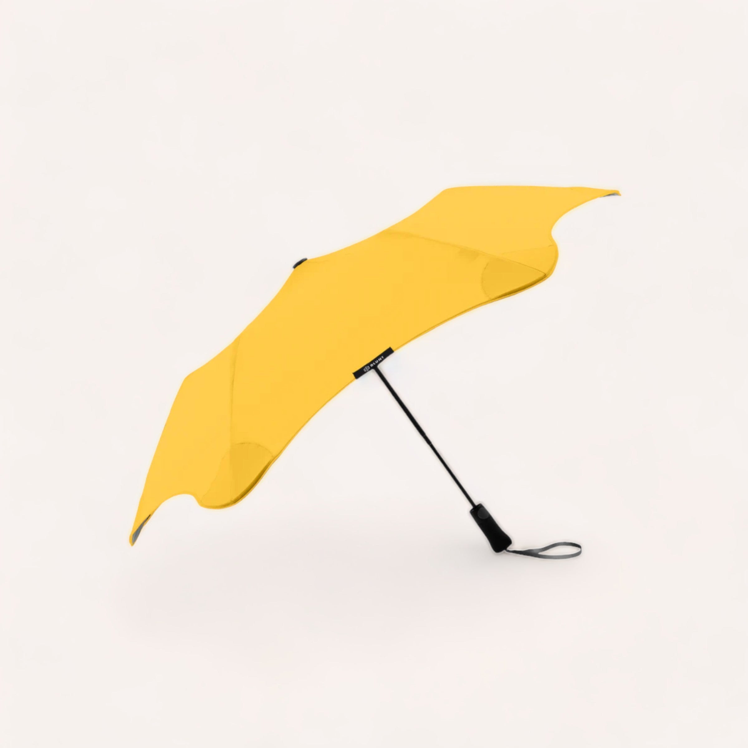 A vibrant yellow BLUNT Metro umbrella lying open against a white background.