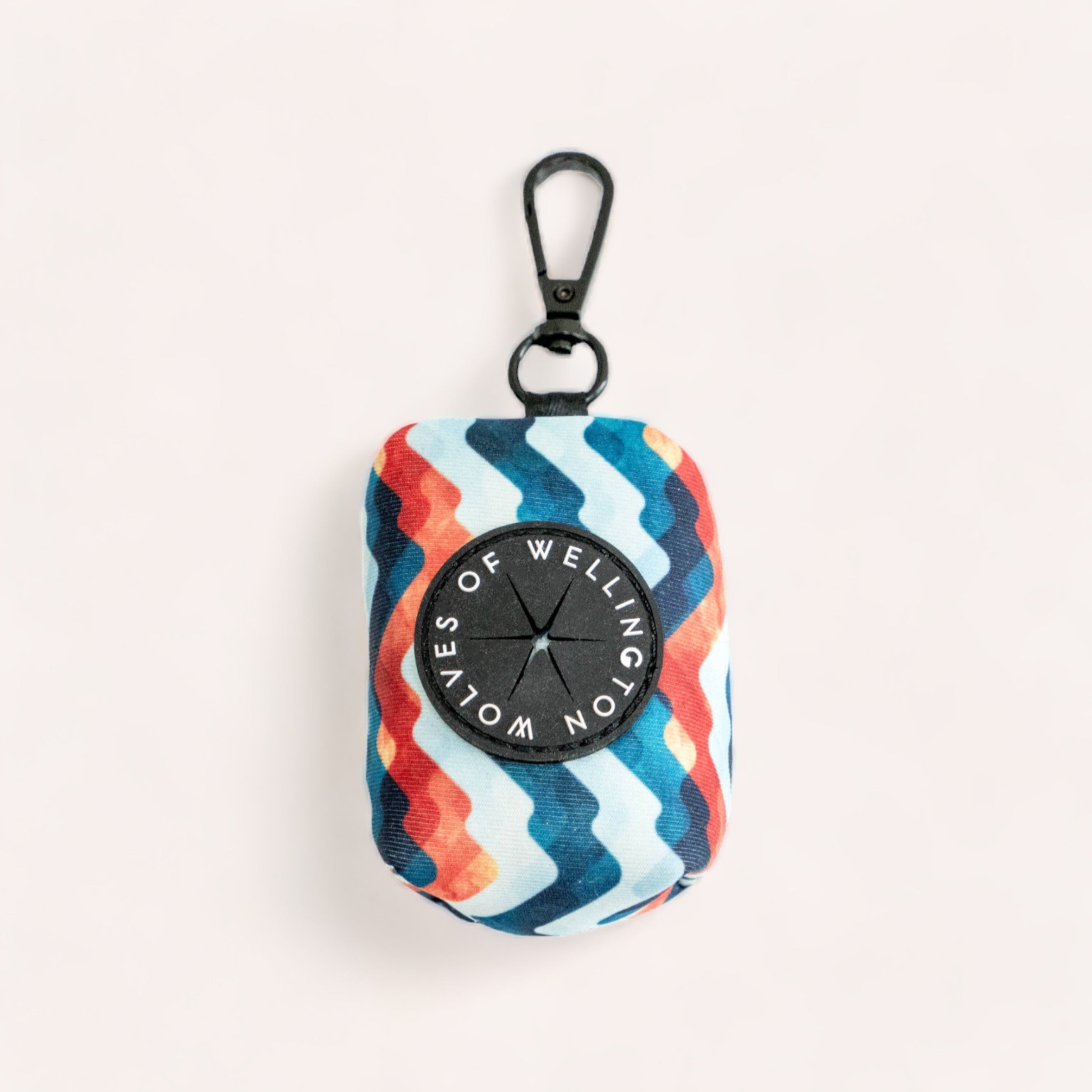 A colorful striped Maverick Poop Pouch with a compass design in the center, designed for holding dog poop bags, and a carabiner attached, lying on a plain background by Wolves of Wellington.