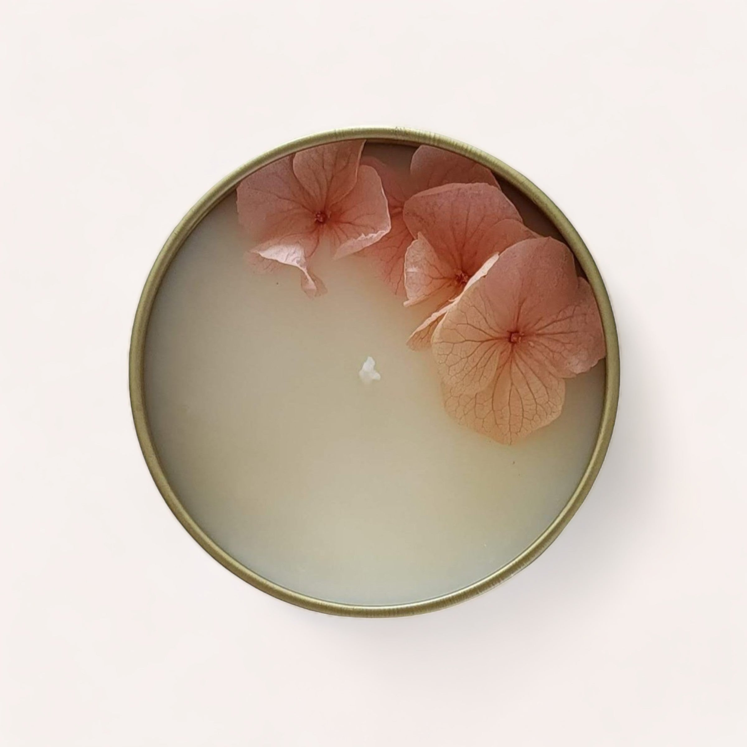 Strawberries + Champagne Candle adorned with delicate pink hydrangea petals on a creamy wax surface, encased in a reusable gold tin, evoking a sense of tranquility and relaxation by Wix's Lane Co.