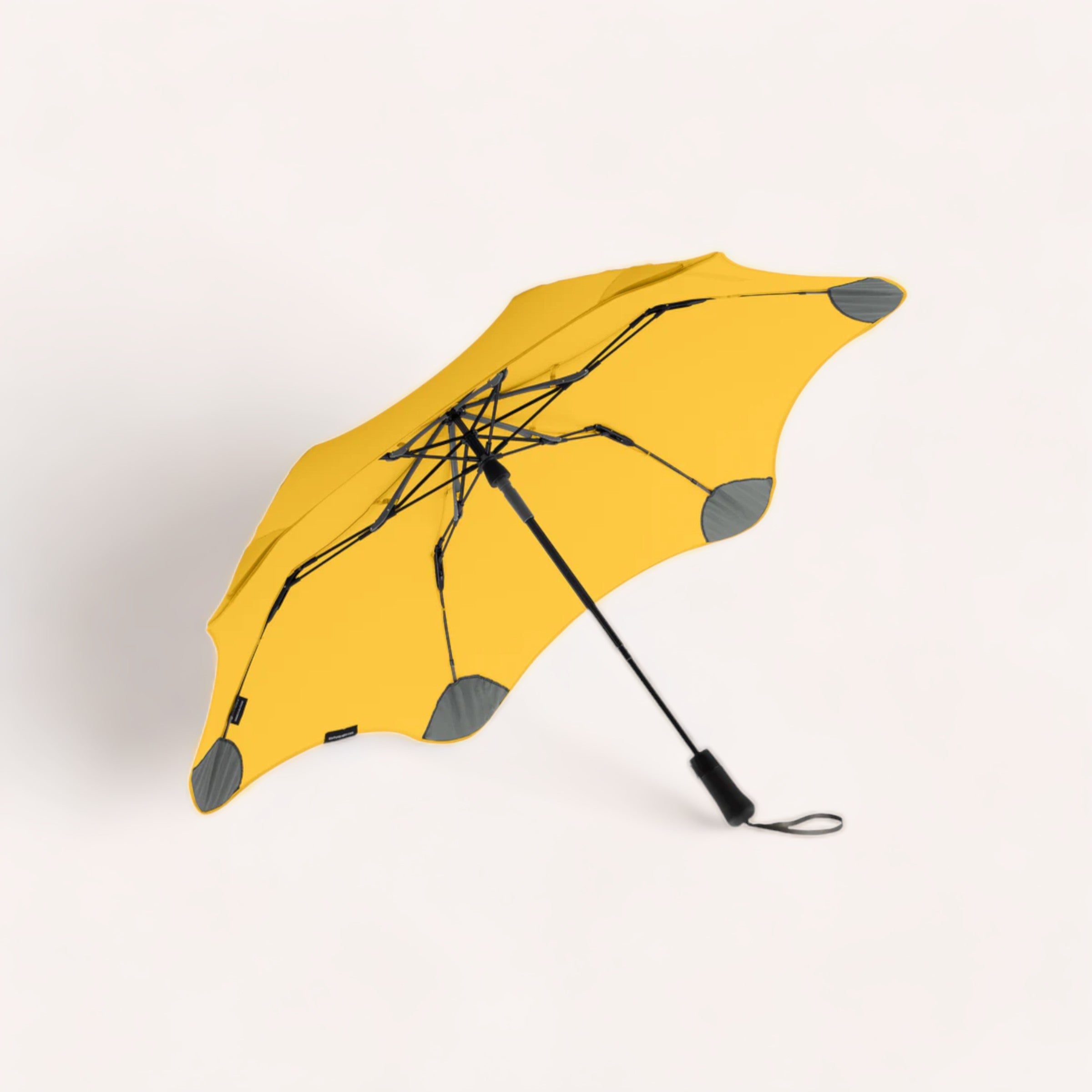 A bright yellow BLUNT Metro umbrella, designed with an auto-open canopy for the urban dweller, turned inside out, possibly by strong winds, lying against a plain white background.