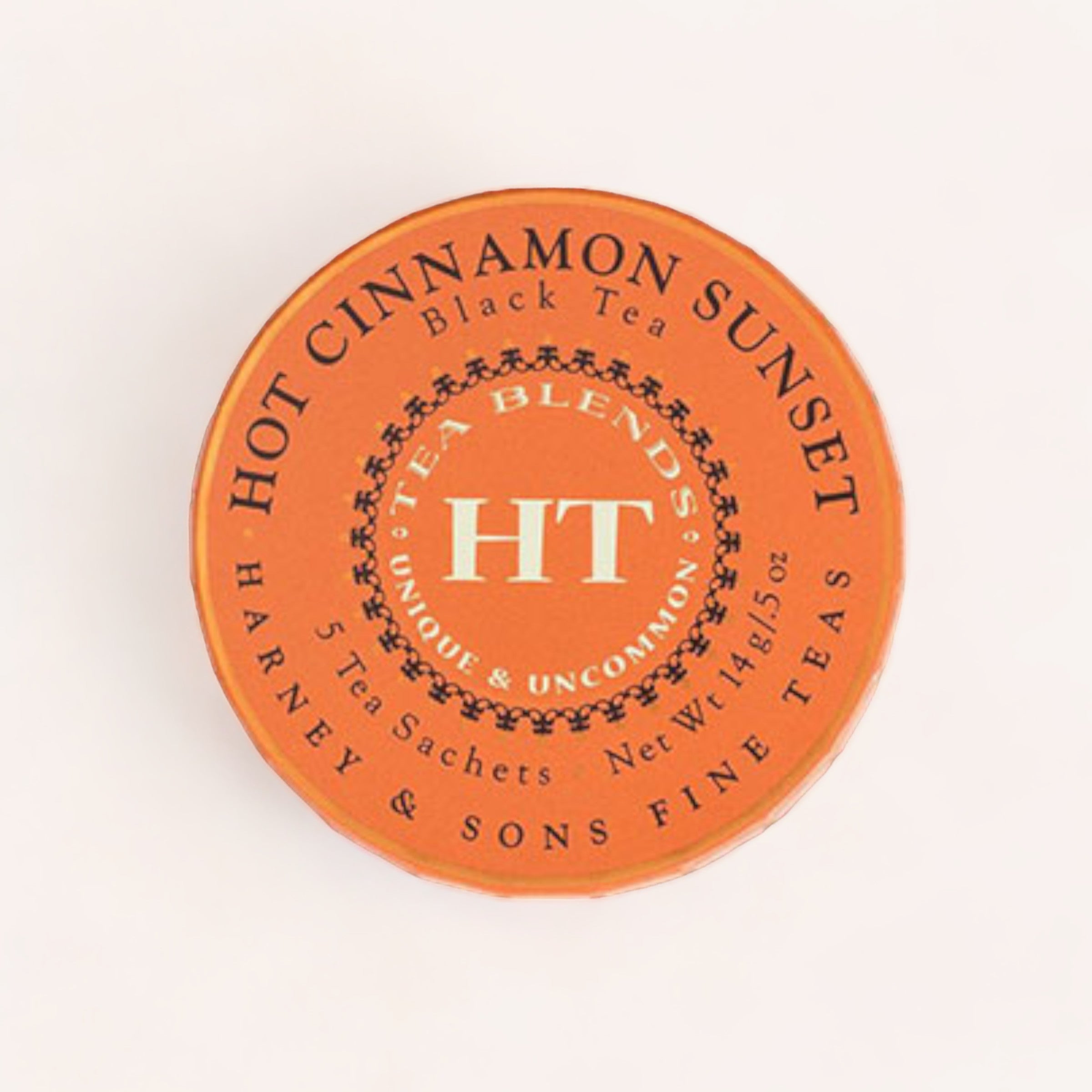 A round, orange tin lid labeled "Hot Cinnamon Sunset Tea Tagalong" from Harney & Sons, emphasizing its unique and uncommon loose leaf tea blend.