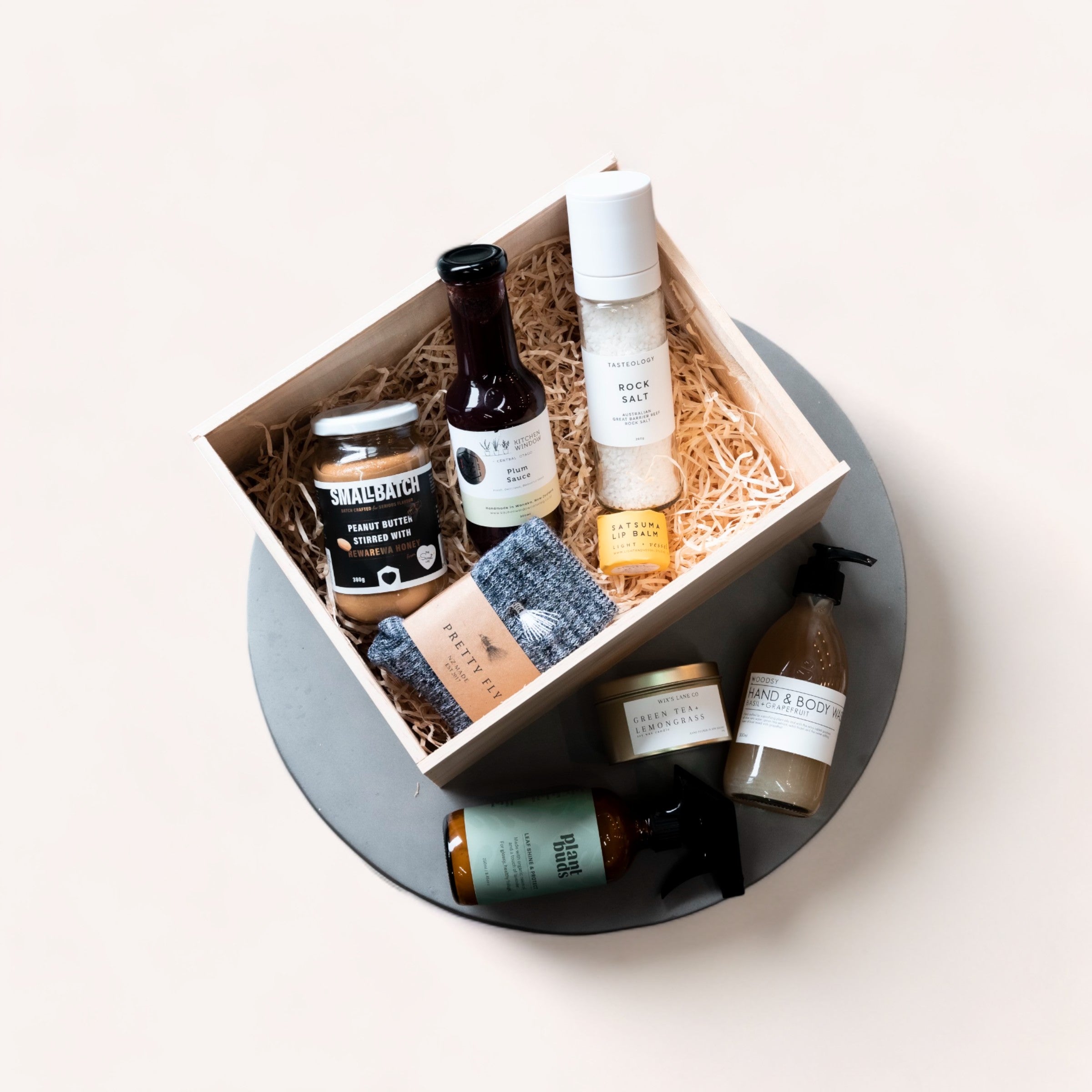 A curated Build Your Own Giftbox from giftbox co. filled with luxury items, including skincare products and gourmet food, beautifully arranged on a round concrete plate against a neutral background, accompanied by a personalised handwritten card.