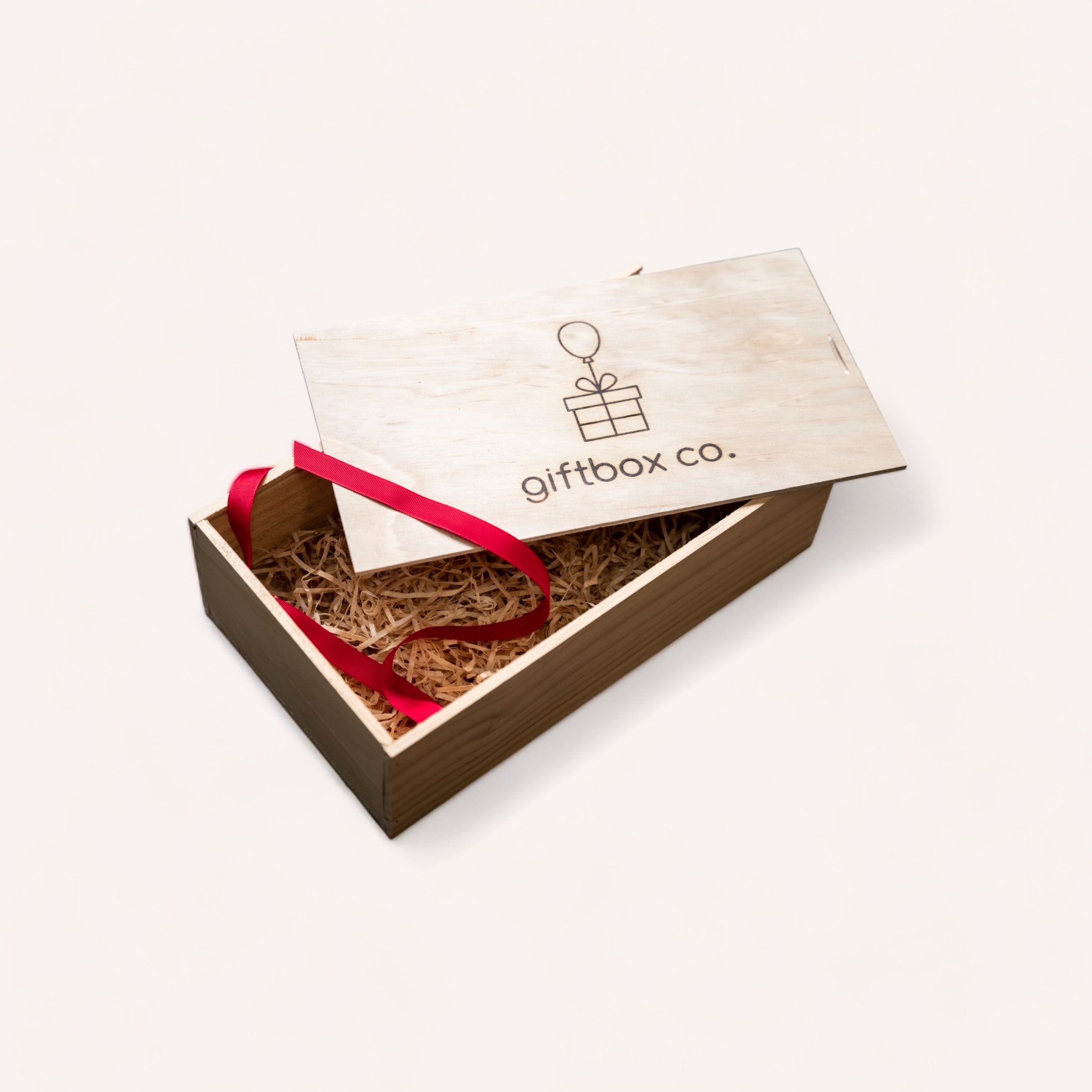 An elegant Build Your Own Giftbox from giftbox co. , with a sliding lid, adorned with a red ribbon, and containing protective straw filler, ready for a thoughtful present and a personalised gift.