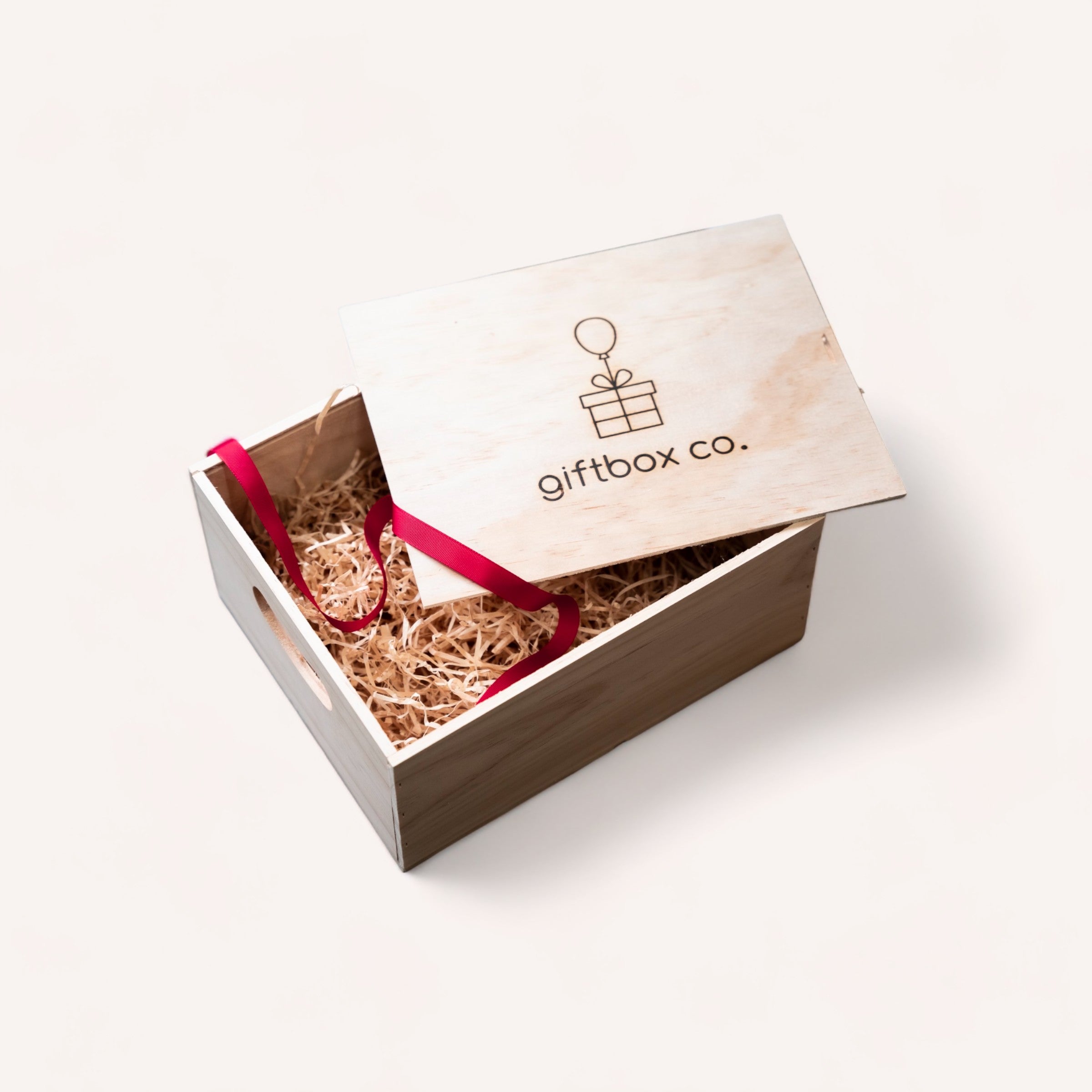 An elegant Build Your Own Giftbox with a sliding lid, branded with "giftbox co." and a ribbon accent, is partially open to reveal decorative filler material and a personalised gift inside, suggesting a thoughtful present.