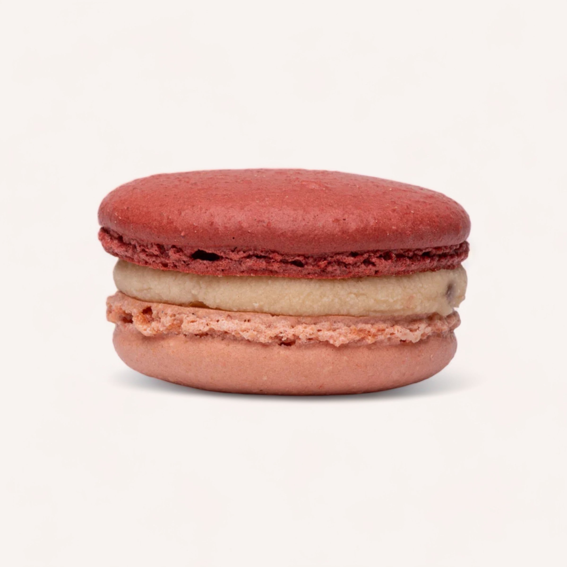 A handmade macaron with a red shell and a creamy filling, depicted against a white background in Christchurch, New Zealand from the Box of 6 Macarons by J'aime les Macarons.