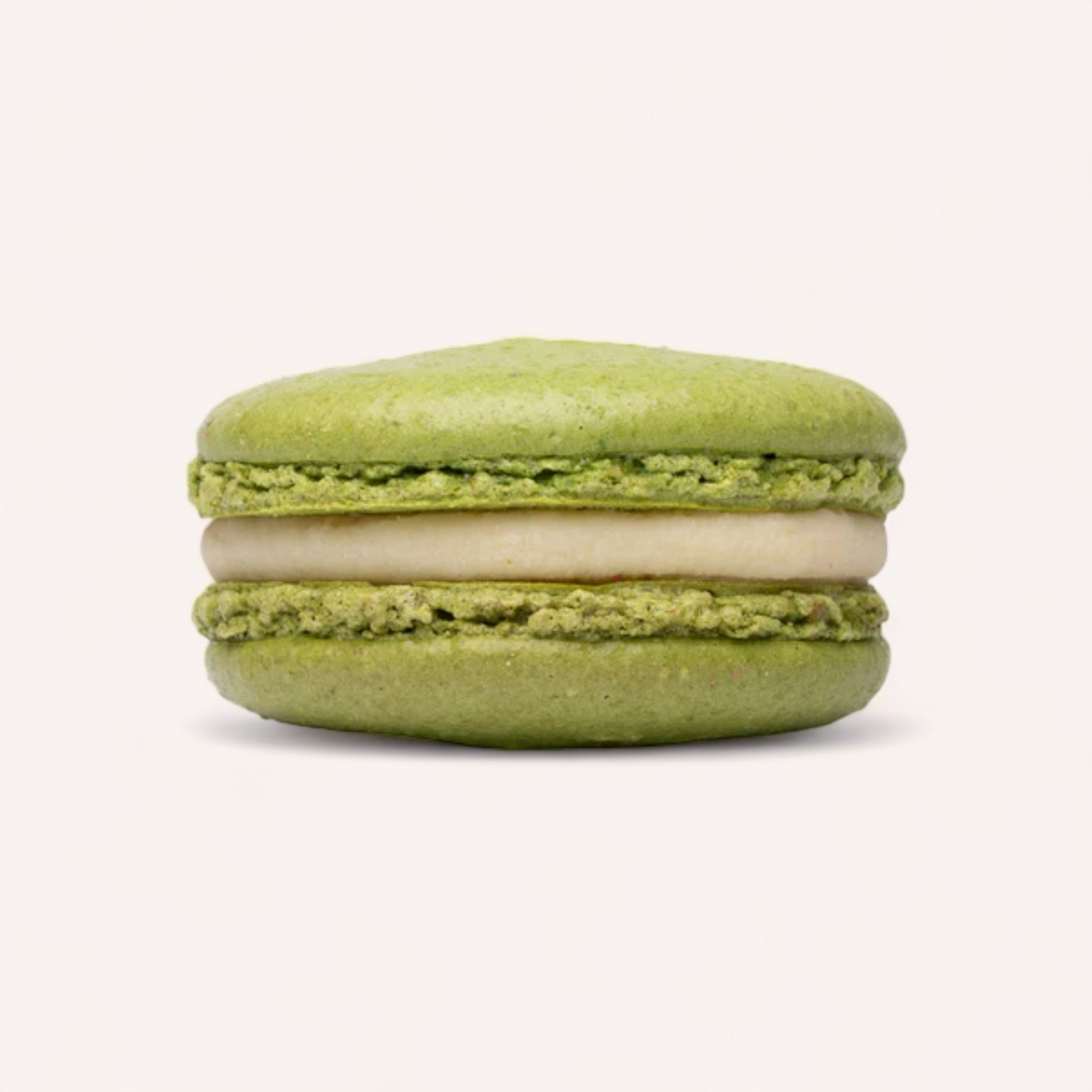 A single handmade green Box of 6 Macarons by J'aime les Macarons with a cream filling isolated on a white background.