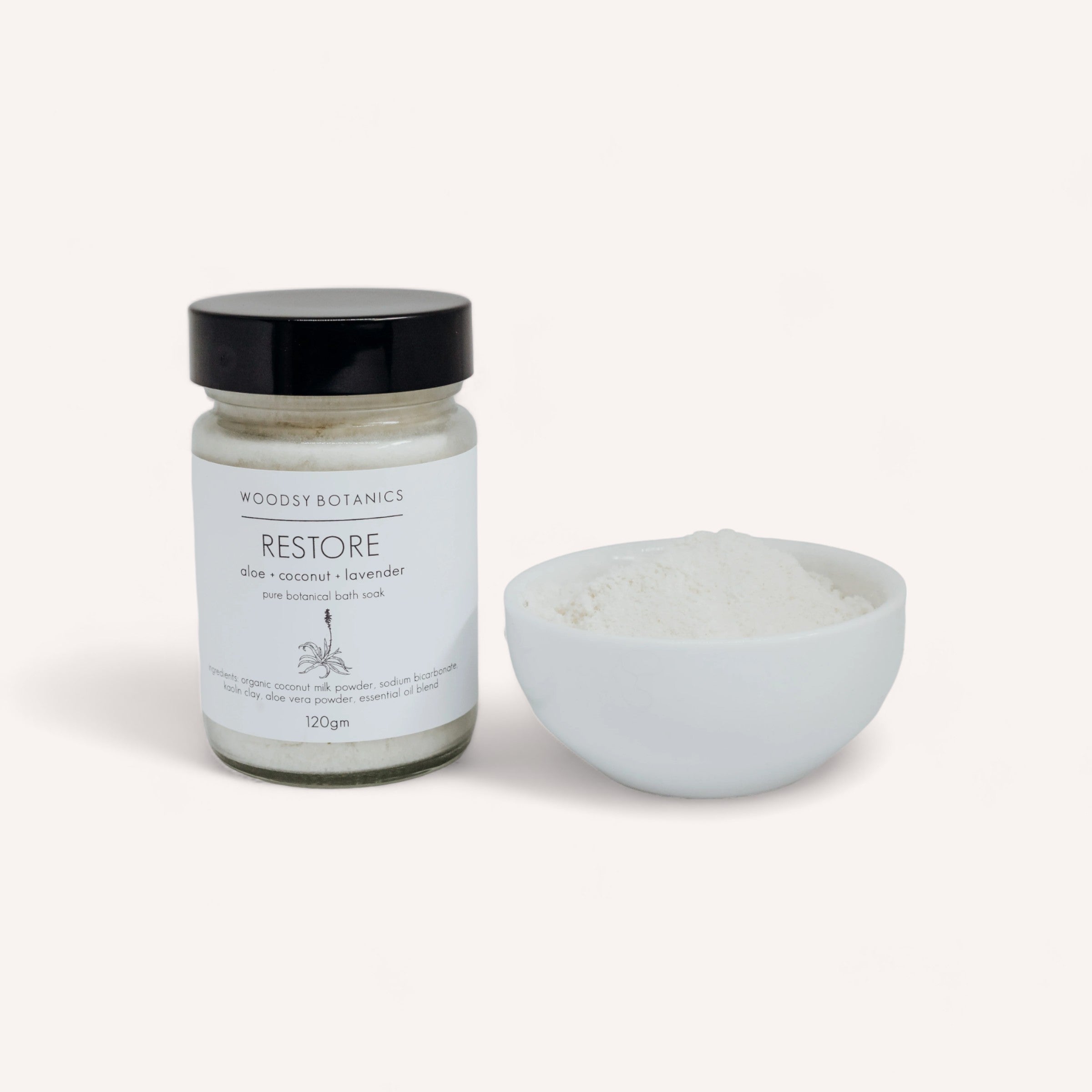 A jar of "Bath Lovers Gift Set by Woodsy Botanics" with rose, coconut, and lavender beside an open white bowl filled with the salts, isolated on a white background.