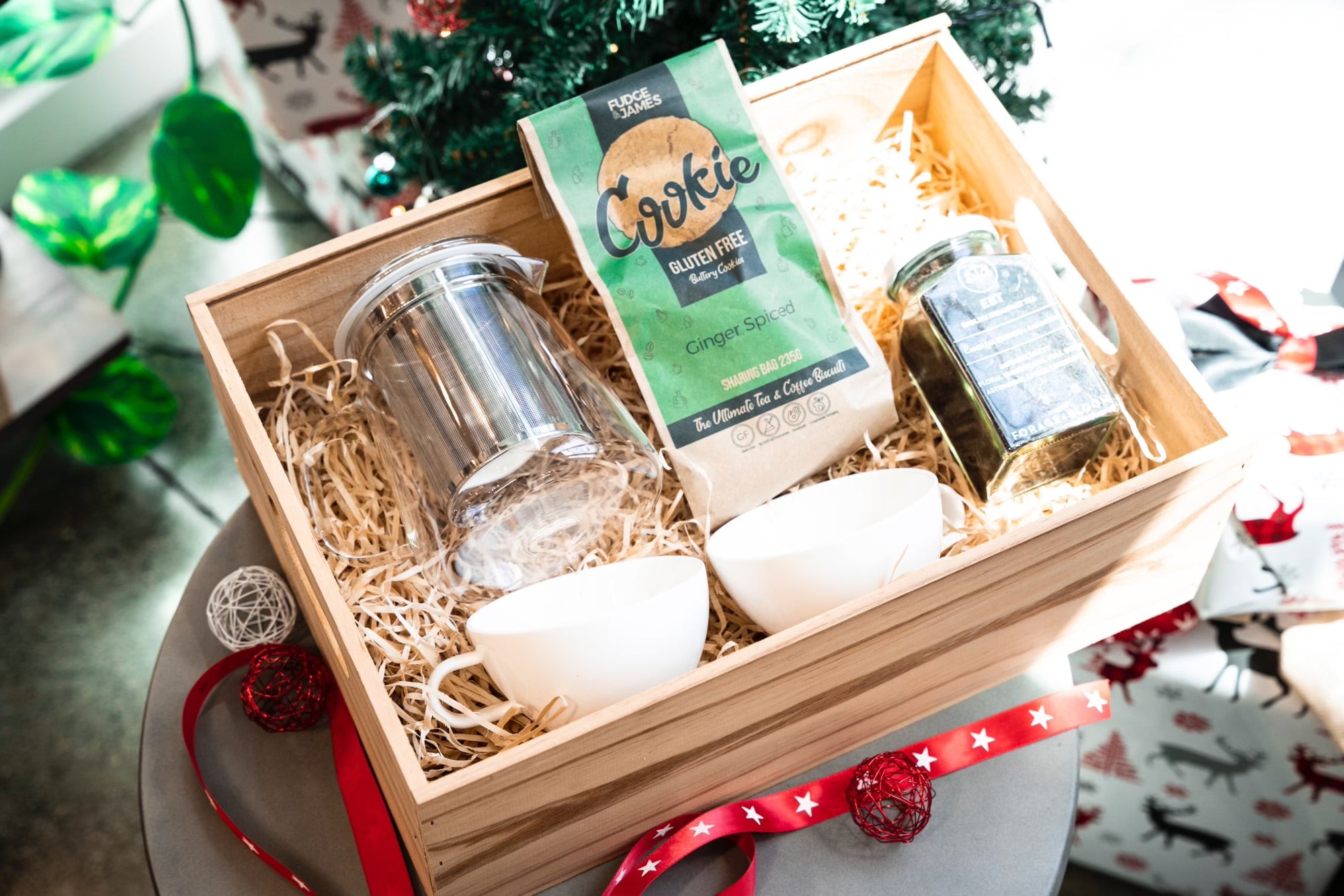 A festive Tea for Two holiday gift box by giftbox co. featuring gourmet loose leaf tea, a pair of elegant glass cups, and an accompanying glass infuser, thoughtfully arranged on a bed of natural straw and adorned with festive decorations.