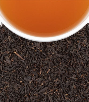 A white bowl filled with Black Cask Bourbon Tea by Harney & Sons, resting atop a bed of loose leaf tea, viewed from above.