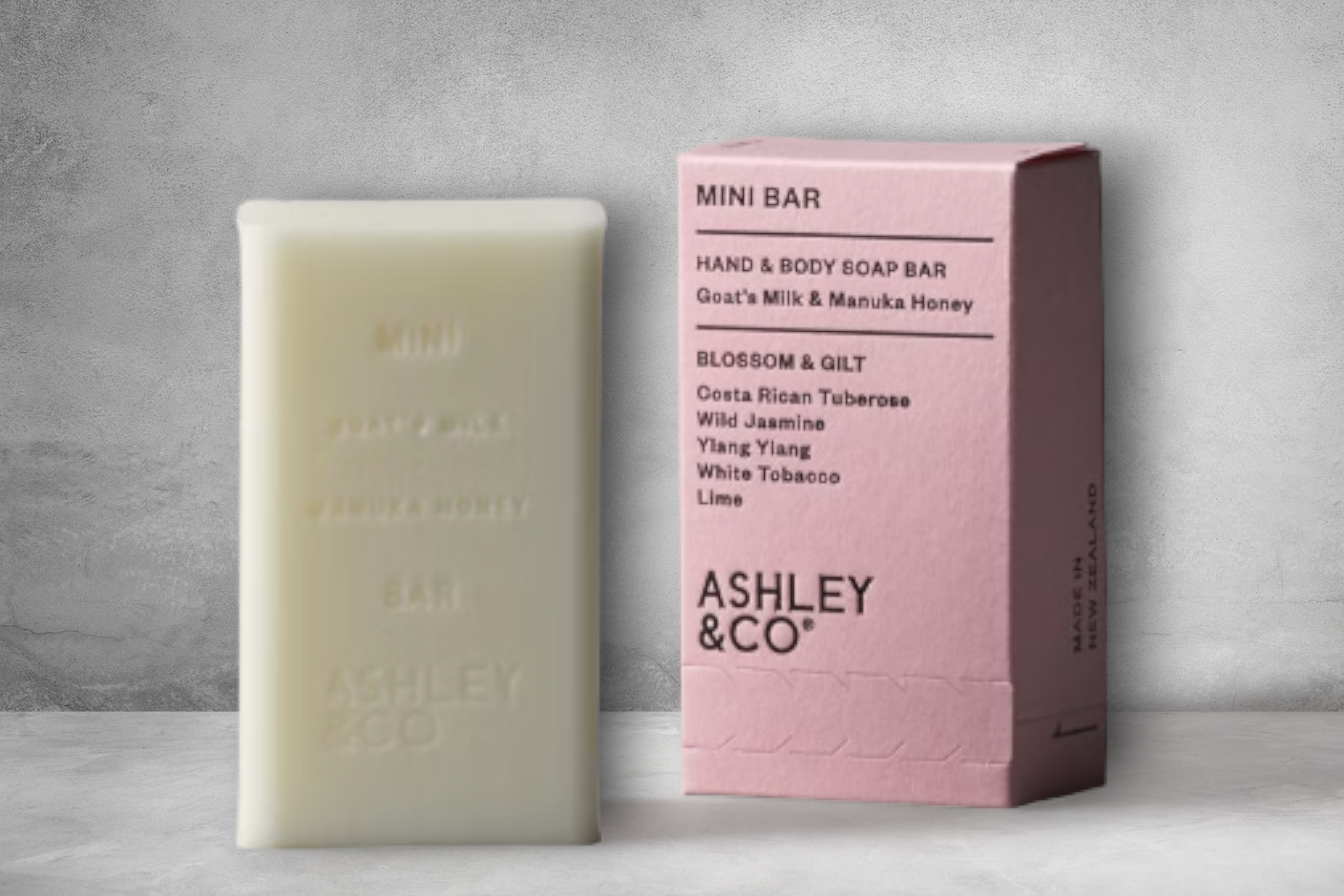 A cleansing bar of Blossom & Gilt Mini Bar by Ashley & Co hand and body soap alongside its stylish pink packaging, highlighting a blend of goats milk and Manuka honey with fragrant botanical notes.