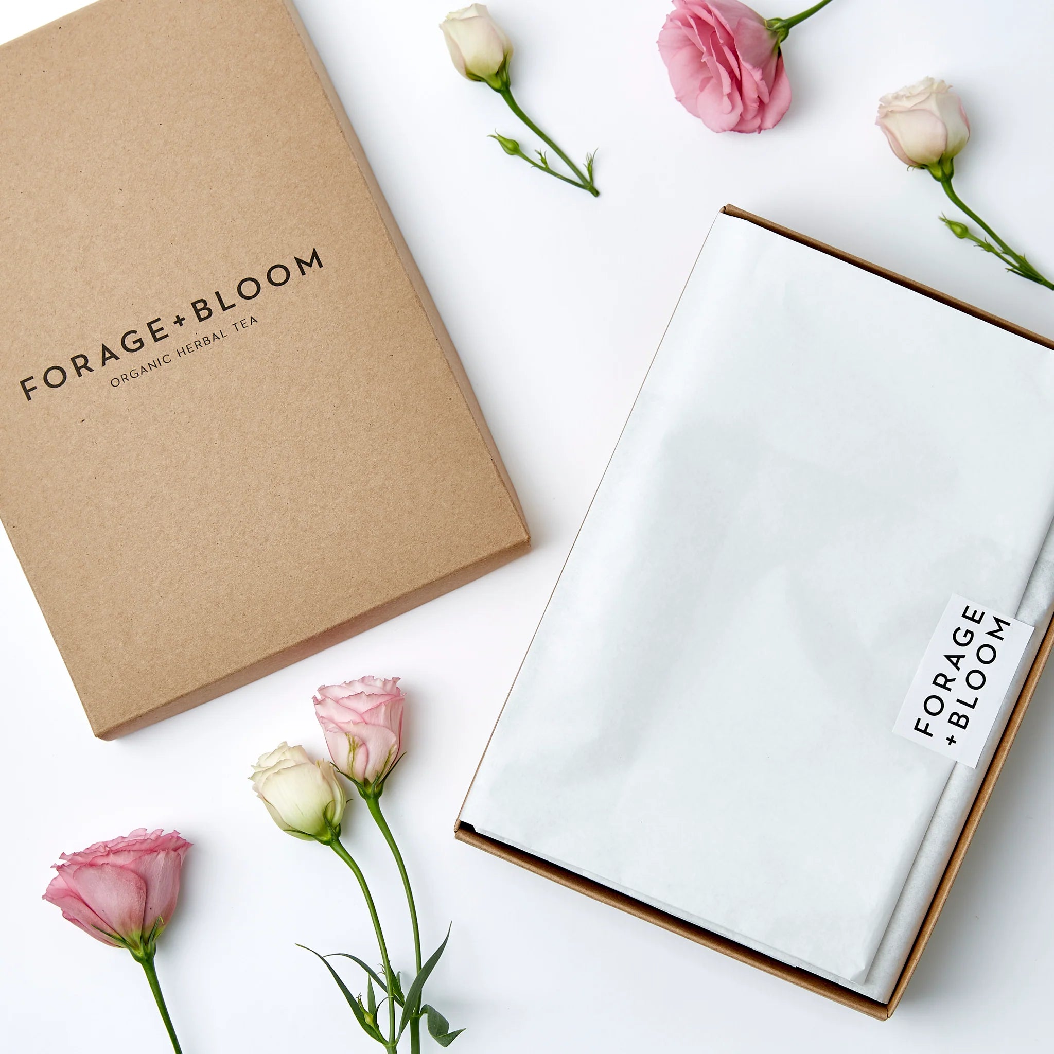 Sentence with product and brand name: Elegant Tea Testing Box Set by Forage + Bloom packaging with a touch of nature: forage + bloom herbal tea blends nestled among delicate pink roses on a clean, white background.
