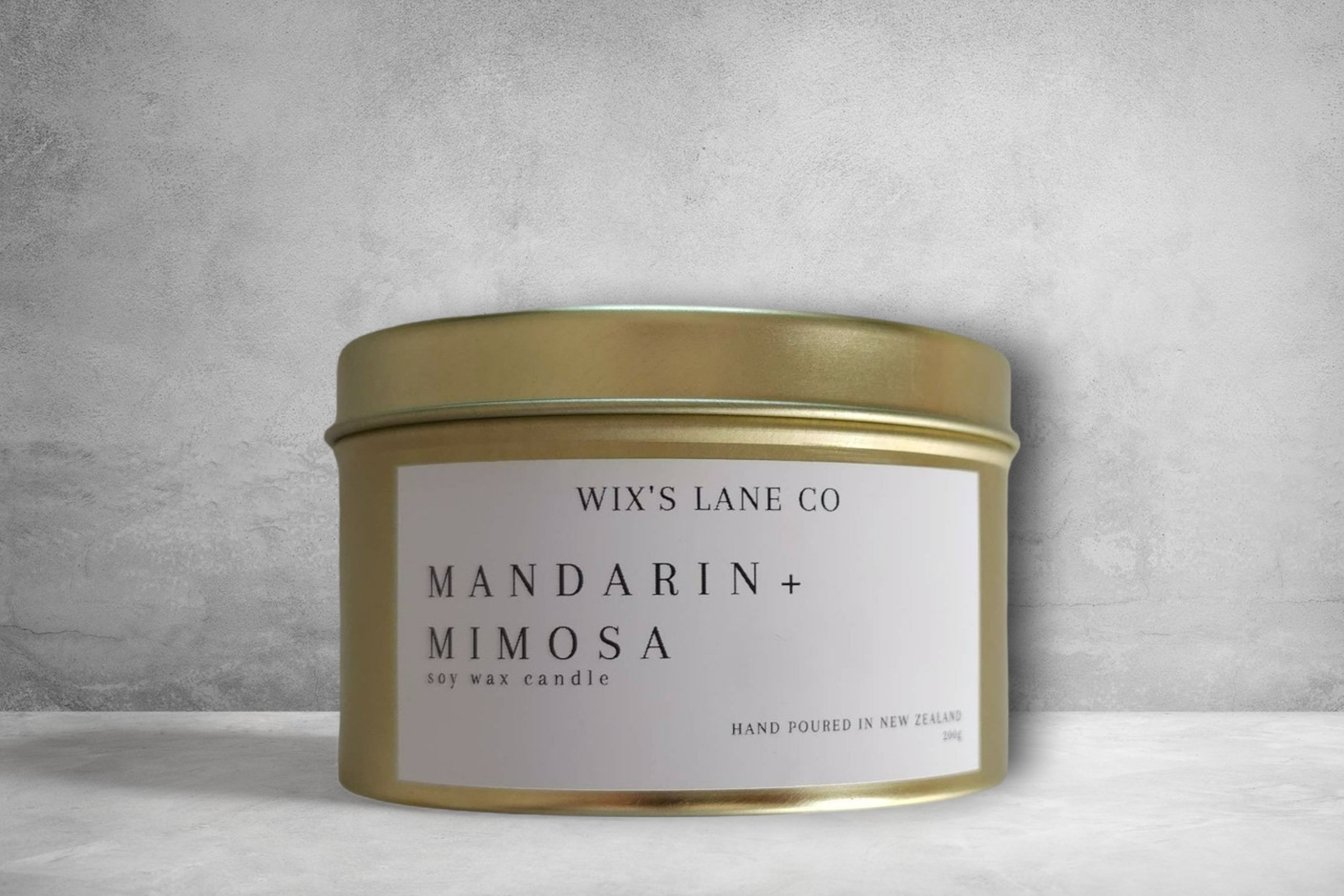 A tranquil golden Mindful Moments soy wax candle by giftbox co. with mandarin + mimosa scent, hand poured in New Zealand, displayed against a textured grey background.