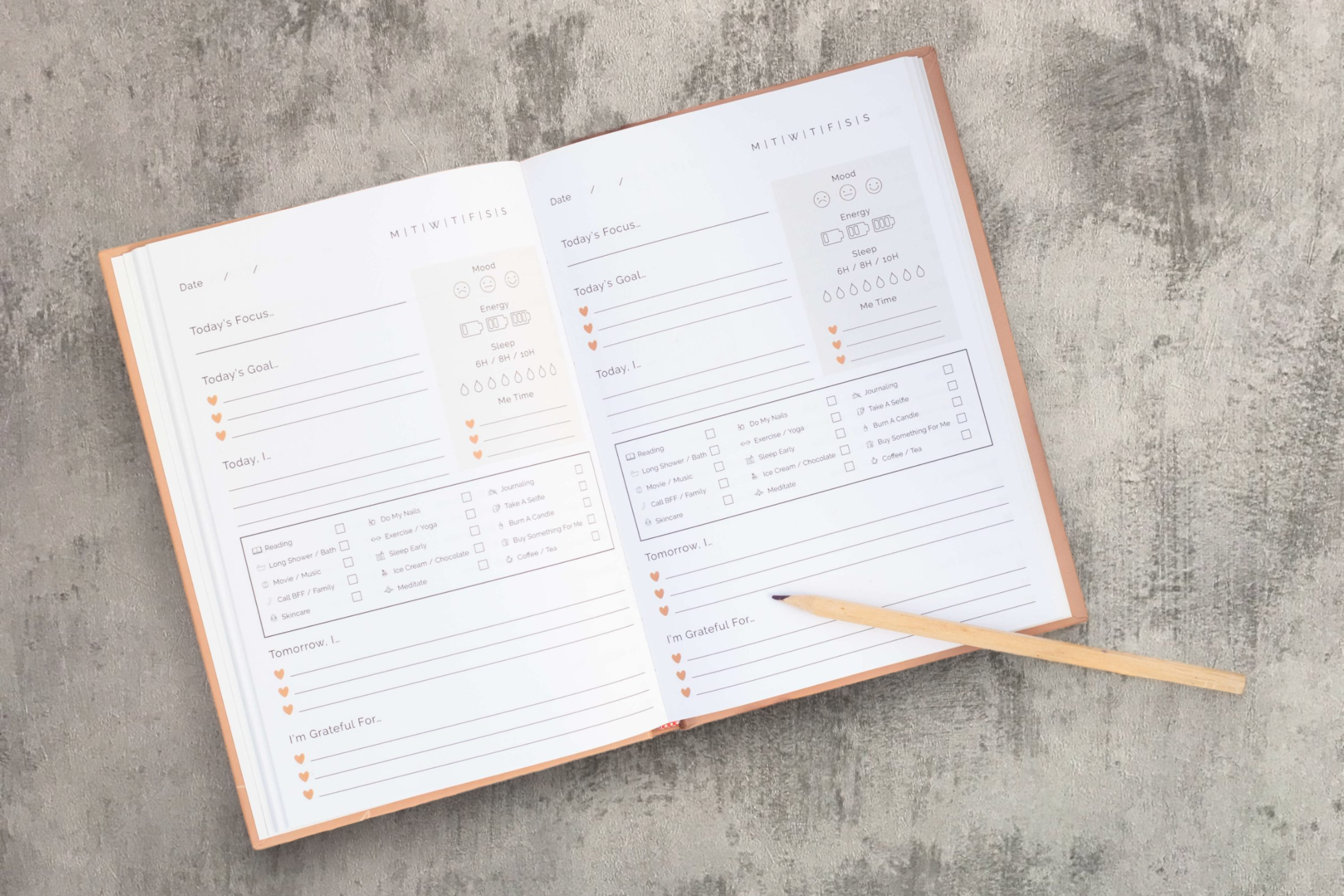 An open Mindful Moments planner with a weekly layout placed on a textured gray background, accompanied by a pencil resting diagonally across it and a tranquil candle, suggesting productivity, organization, and reflection.