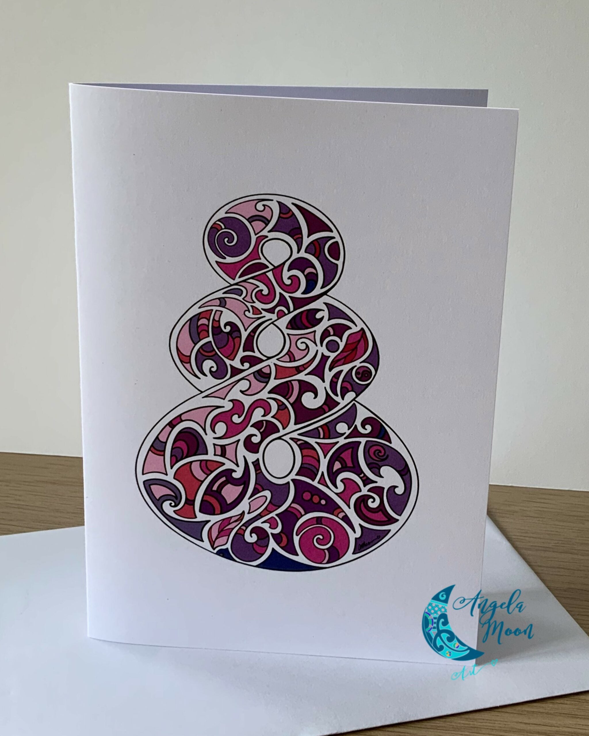 A Pink Pikorua Card featuring an intricate, purple filigree number "8" design on a white background, with the artist's signature "angela moed" at the bottom right corner. This Angela Moon Art product